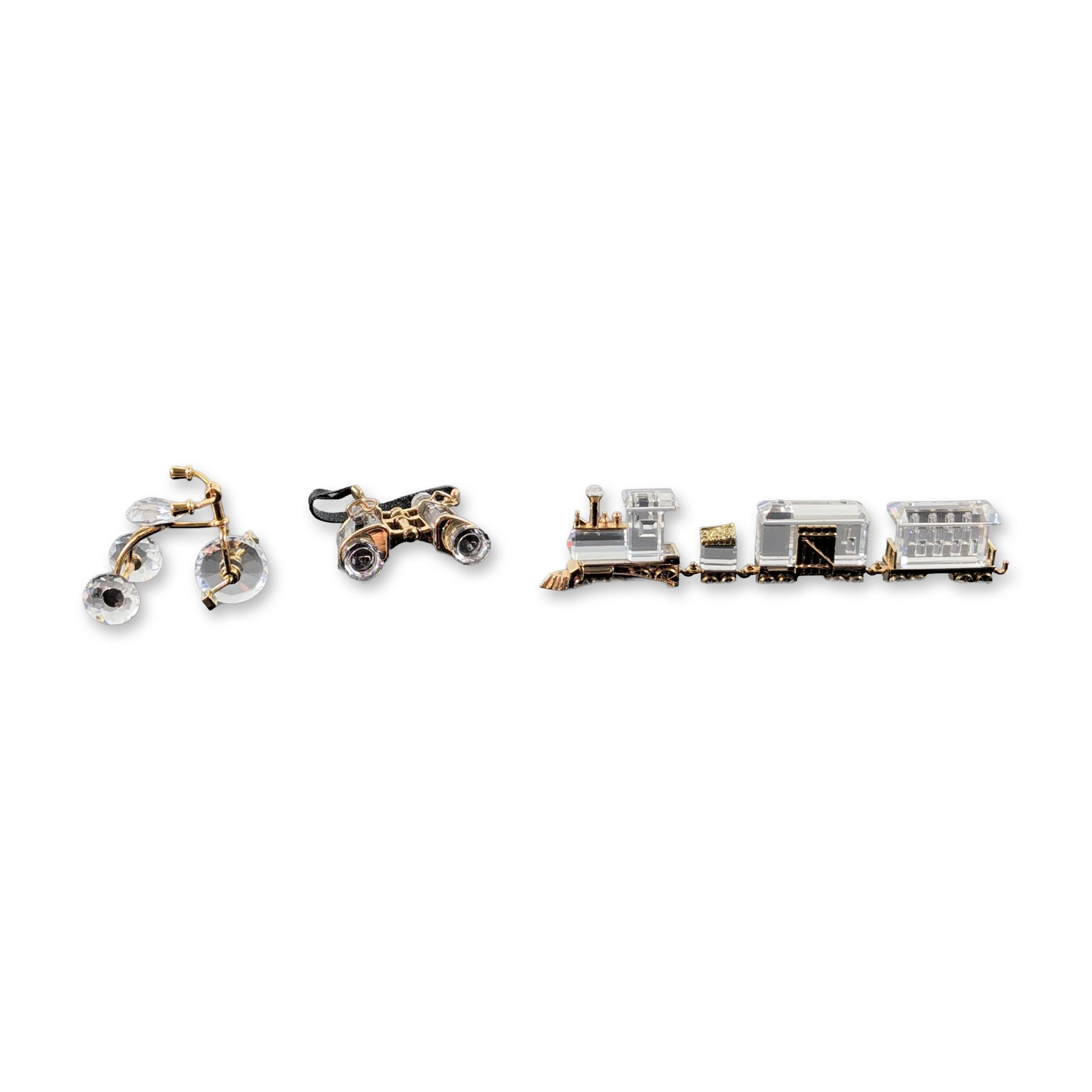 3pc Swarovski Crystal Memories Gold-Toned Miniatures: Three Swarovski Crystal Memories miniatures in faceted clear lead crystal and gold-toned metal, featuring three train cars, binoculars with a black flexible strap, and a tricycle. Each piece is marked