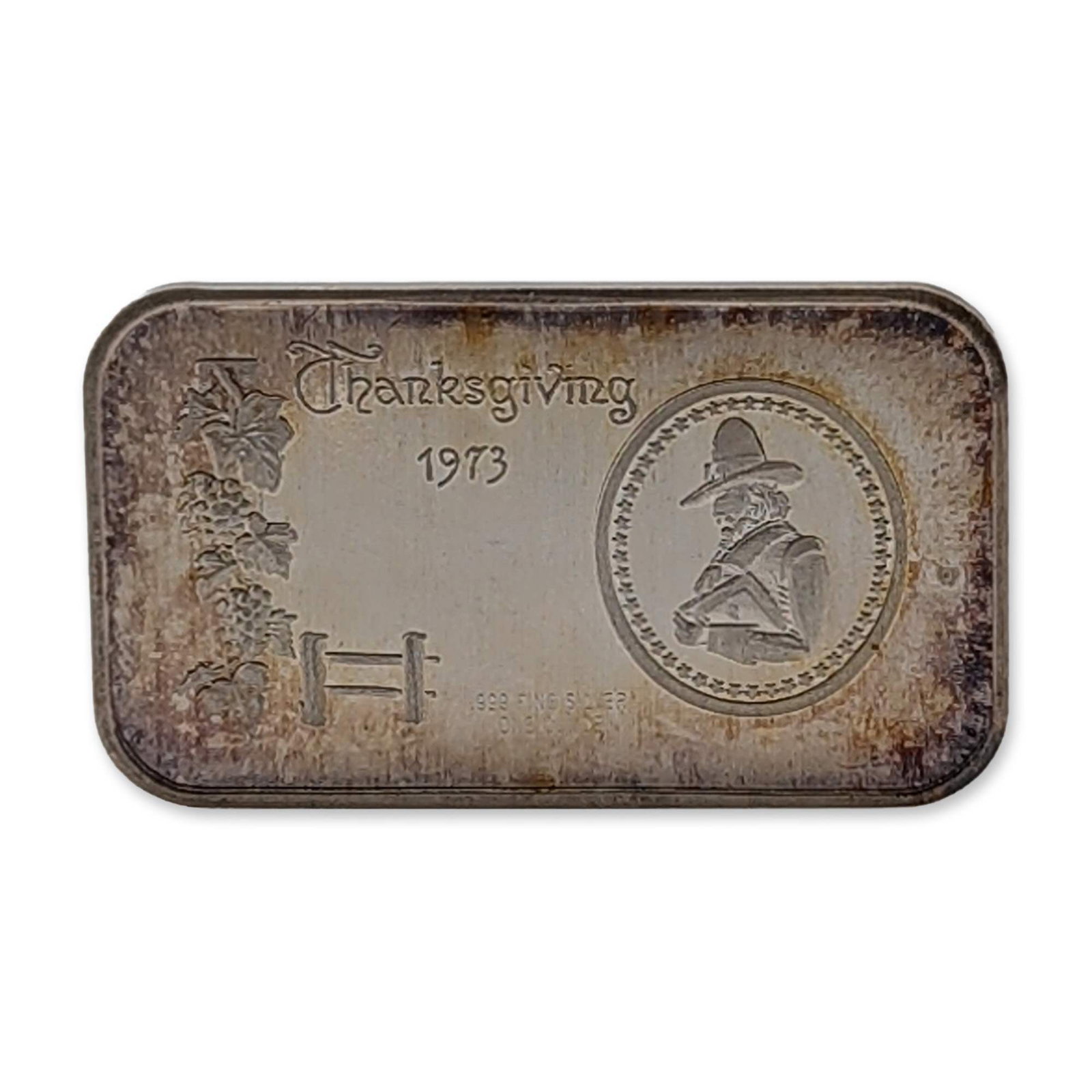 Madison Mint 1973 Thanksgiving .999 Silver Bullion Bar: Madison Mint. 1973 Thanksgiving silver art bar struck in .999 fine silver. The obverse features a central circular medallion with a Pilgrim profile, positioned above a grapevine motif and a stylized m