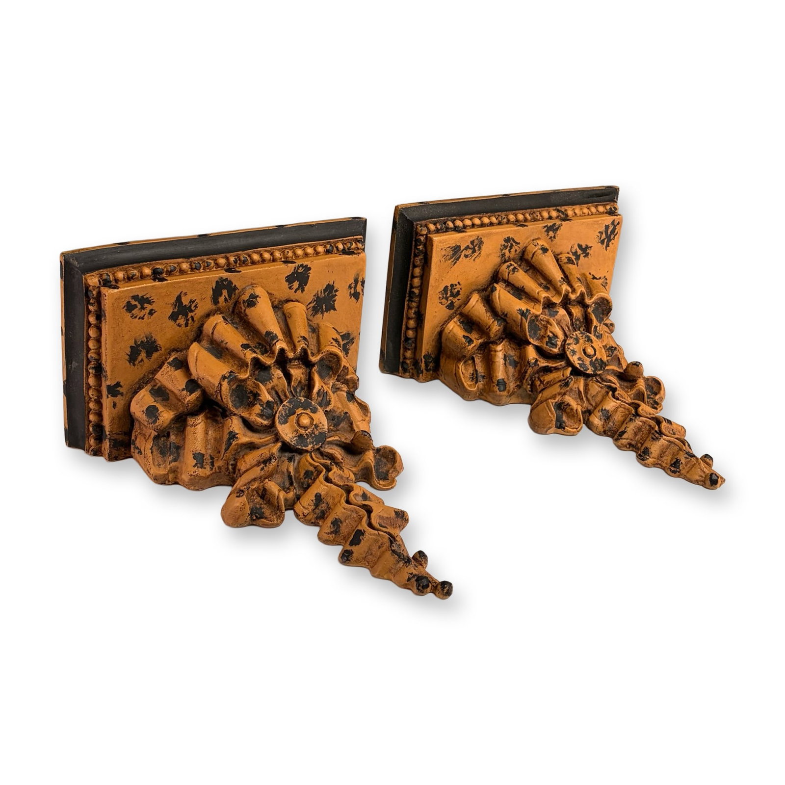Pair of Hollywood Regency Style Composite Wall Shelves: Pair of wall shelves in cast composite resin, featuring an ornate design with tiered ruffled ribbon-work and a central rosette medallion. Each bracket is set on a stepped rectangular base with a