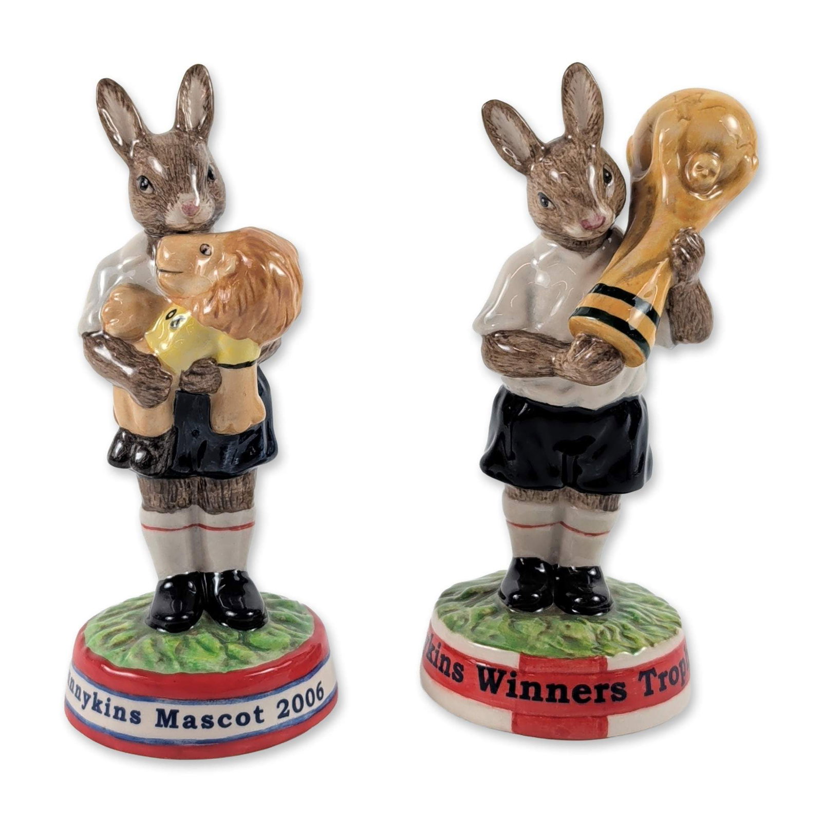 2pc Royal Doulton Bunnykins 2006 World Cup Figurines: Royal Doulton hand-painted ceramic Bunnykins figurines produced for the 2006 FIFA World Cup. The lot comprises "Winners Trophy 2006" (DB 409) and "Mascot 2006" (DB 407), each depicting a rabbit in a s