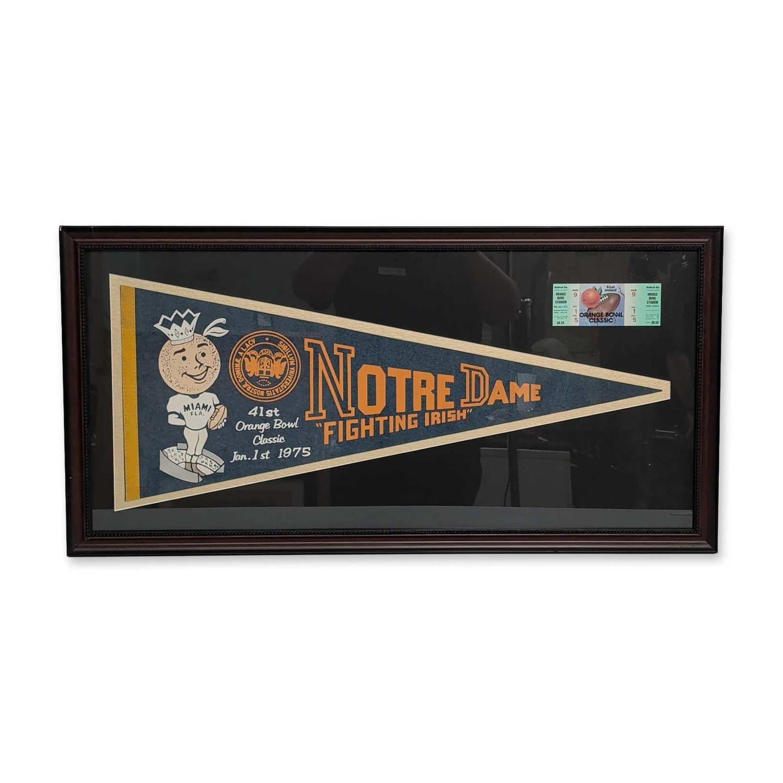 Commemorative Framed 1975 Orange Bowl Notre Dame Pennant and Ticket: Commemorative college football display featuring memorabilia from the 41st Orange Bowl Classic held on January 1, 1975. The collection includes a full-size navy blue felt pennant with gold silkscreene