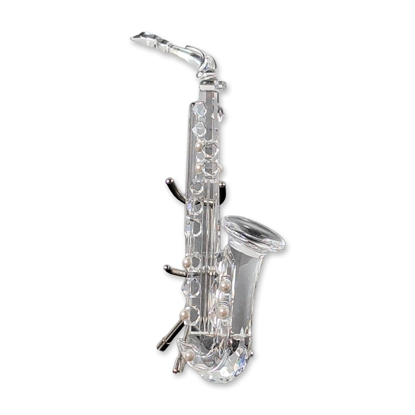 Swarovski Crystal Saxophone with Stand: Swarovski. Miniature saxophone from the Crystal Melodies collection in faceted clear lead crystal, accented with cream-colored spherical faux-pearl keys. Includes original black-coated metal tripod di