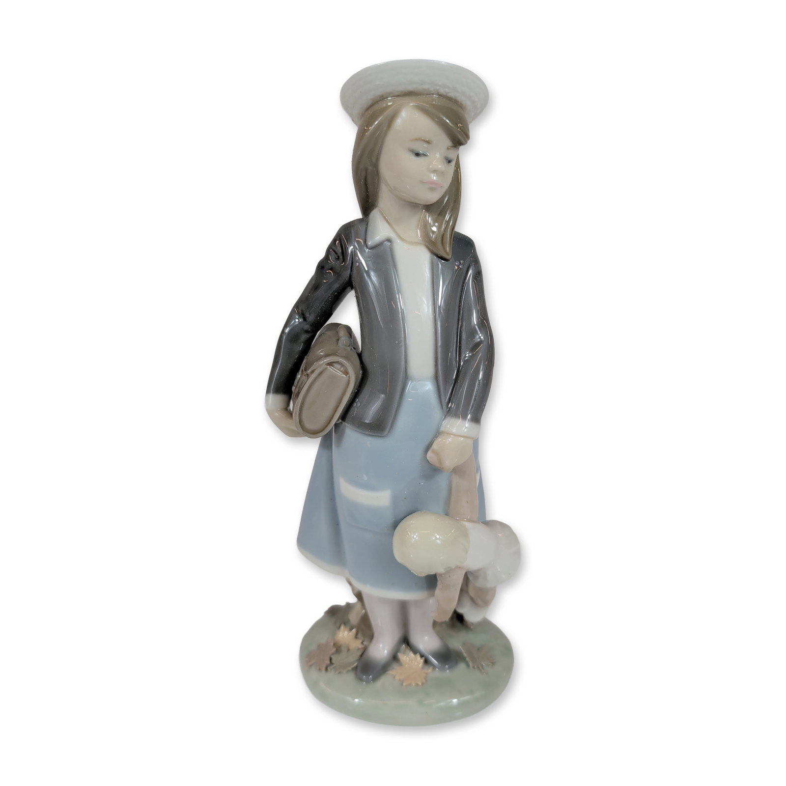 Lladro 5218 Autumn Glazed Porcelain Figurine: Lladro, Spain. Autumn glazed porcelain figurine, model number 5218, depicting a young girl in a grey overcoat and light blue skirt with a white hat, carrying a small tan handbag and a white poodle. Th