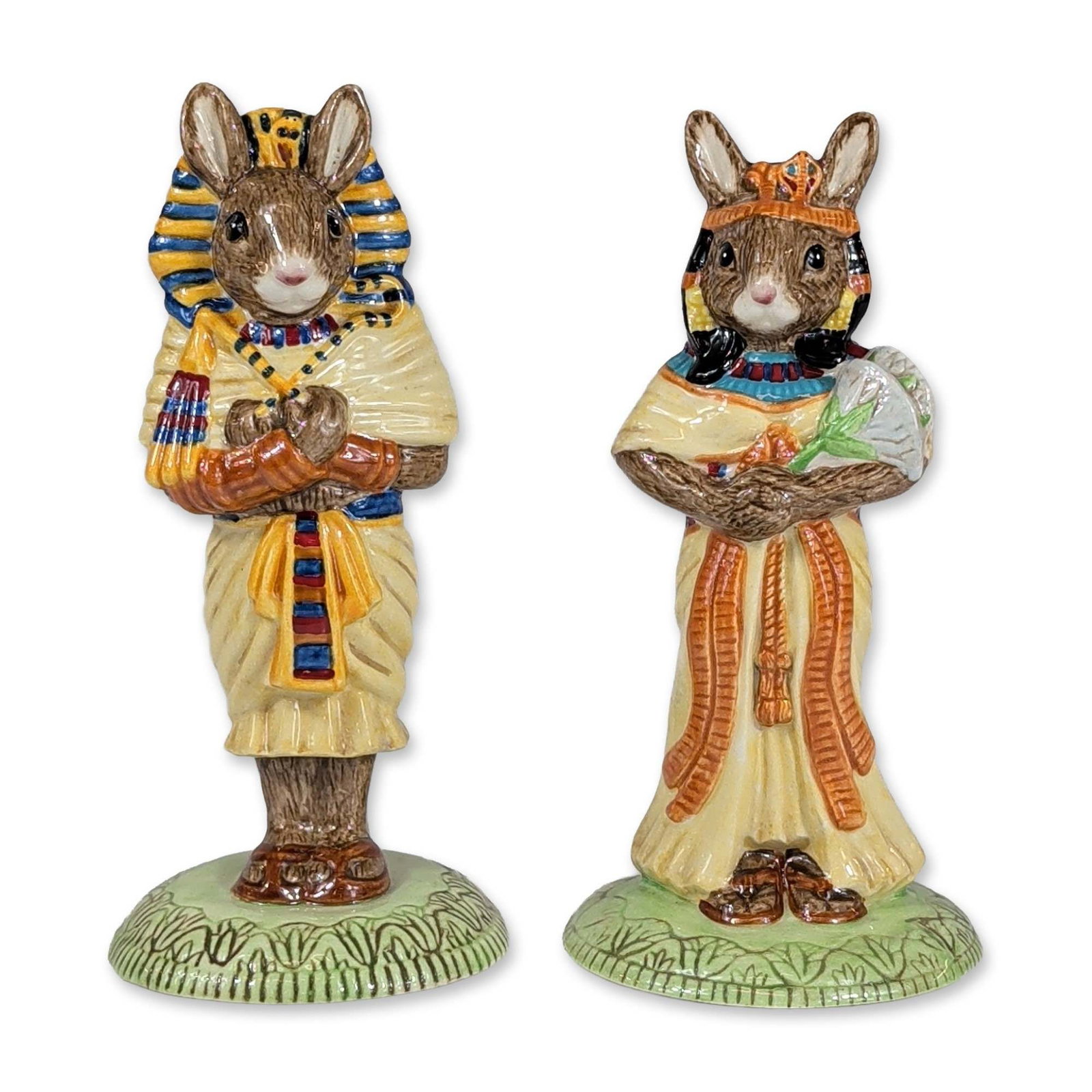 Royal Doulton Bunnykins Egyptian Ceramic Figurines: Royal Doulton. Pair of glazed ceramic figurines from the Bunnykins series with an ancient Egyptian theme, including Ankhesenamun (DB 295) and Tutankhamun (DB 296). Ankhesenamun is depicted in a black 