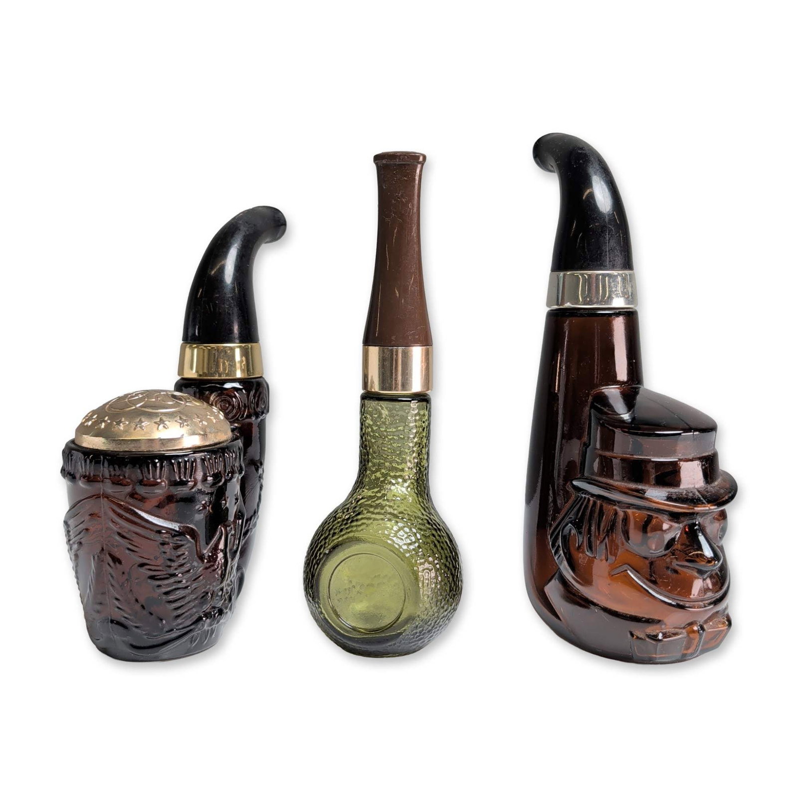 Trio of Avon Vintage Glass Pipe Cologne Bottles: Trio of vintage Avon figural glass aftershave and cologne bottles in the form of tobacco pipes. The group comprises an amber glass character pipe depicting a mariner in relief, a green glass pipe with