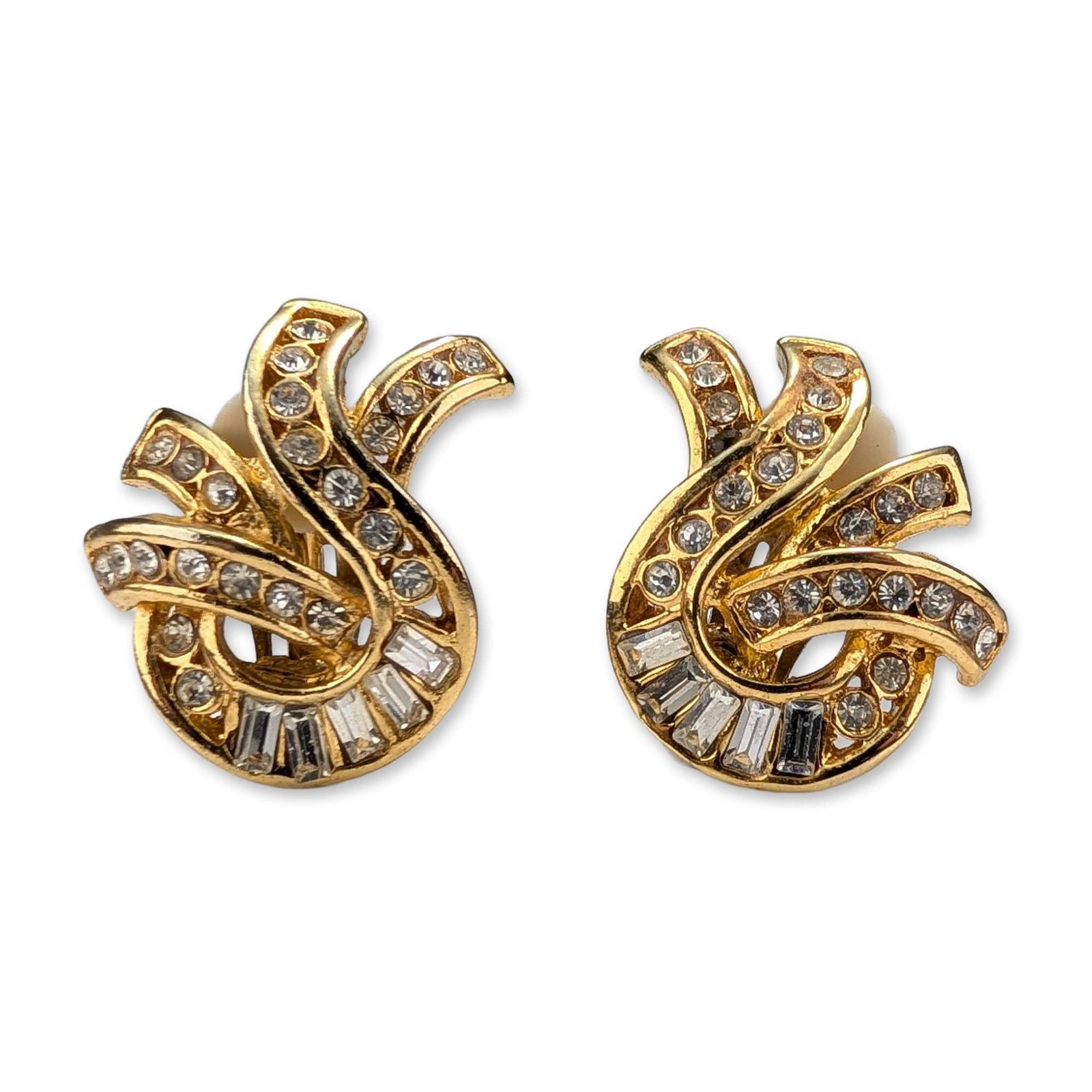 Pair of Gold Toned Rhinestone Swirl Clip Earrings: A pair of vintage gold-toned clip-on costume jewelry earrings. The design features a dynamic abstract swirl or plume motif. The earrings are embellished with pave-set round-cut clear rhinestones and