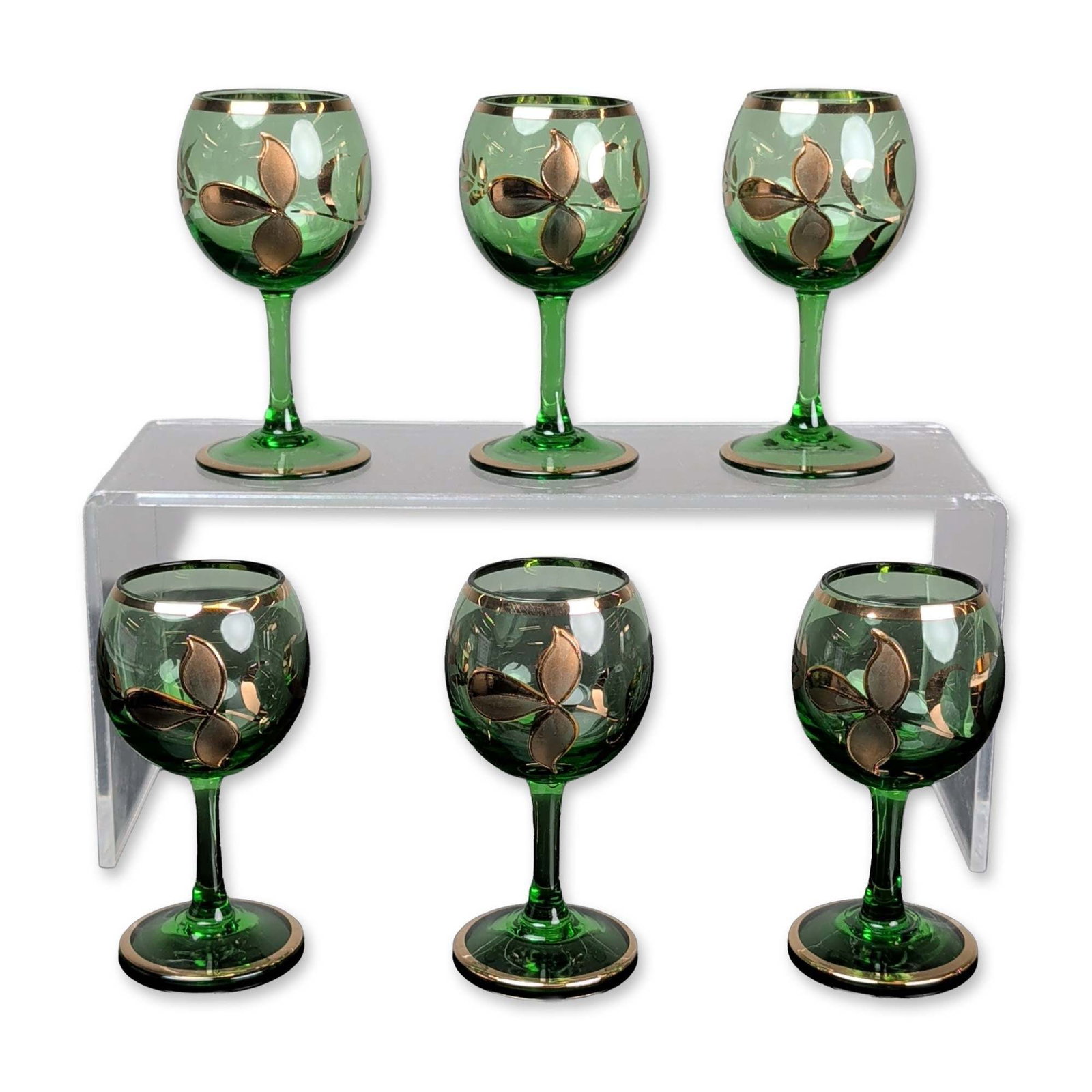 6pc Bohemia Gilded Green Glass Cordials: Vintage set of six cordial glasses in emerald green transparent glass. The bulbous bowls are decorated with hand-applied gilt motifs depicting three-lobed leaves and wheat stalks. Thin gold bands enci