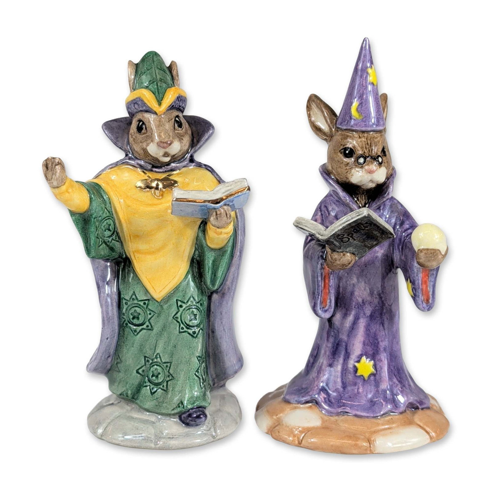 Pair of Royal Doulton Bunnykins Ceramic Figurines: Royal Doulton. Pair of glazed ceramic figurines from the Bunnykins collection. The first, "Wizard Bunnykins" (DB 168), is depicted in a purple star-decorated robe and pointed hat, wearing spectacles a