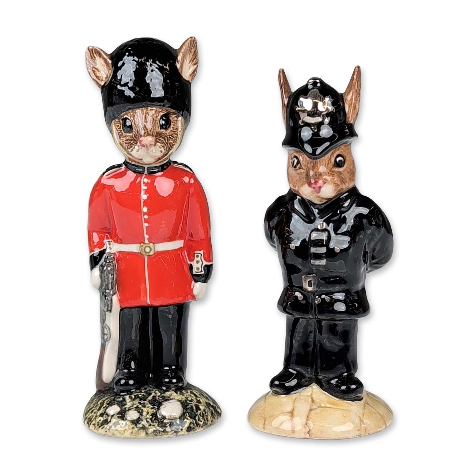2pc Royal Doulton Bunnykins Figurines: Royal Doulton Bunnykins series. Pair of figurines in polychrome glazed ceramic, depicting a British Policeman and a Guardsman. The Policeman, model DB 64, is modeled in a black uniform with a custodia