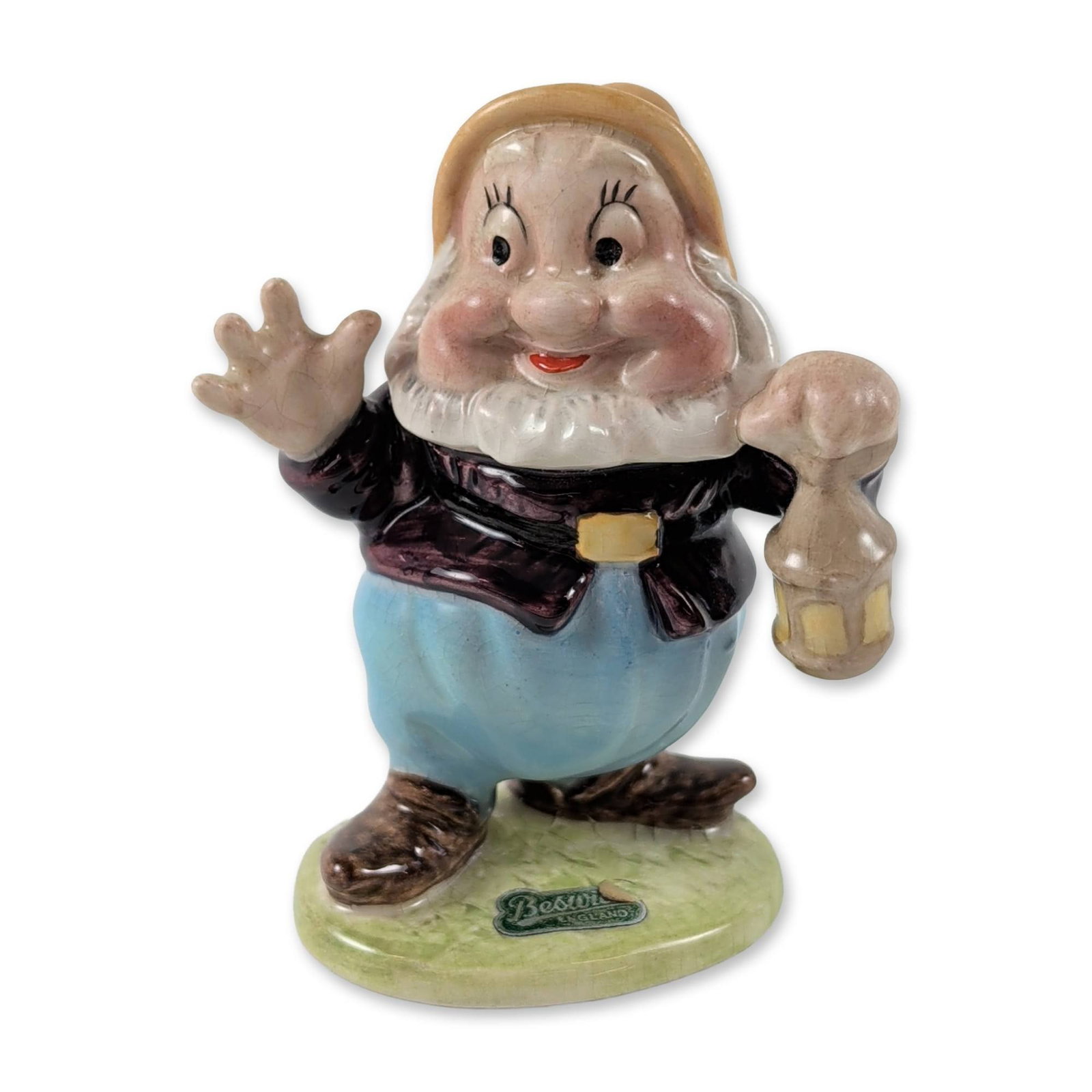 Beswick Disney Happy Ceramic Figurine: Beswick ceramic figurine depicting the character Happy from Walt Disney's Snow White and the Seven Dwarfs. The figure is modeled in a waving pose holding a lantern, wearing a brown jacket, blue trouse