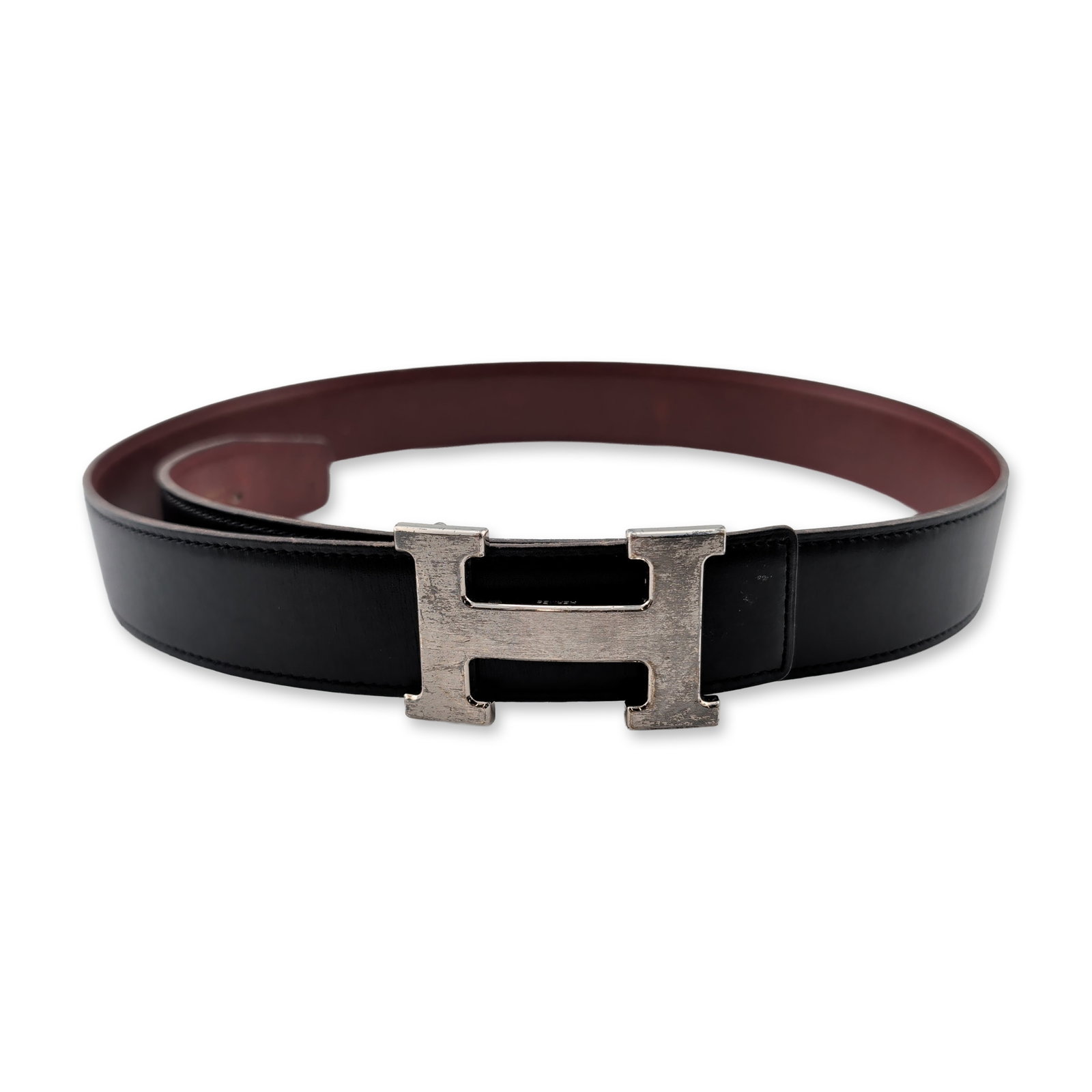 Hermes Reversible Leather Belt with H Buckle: Hermes reversible leather belt with smooth black leather on one side and burgundy leather on the reverse. The item features a signature H buckle in a silver-tone finish. The burgundy side of the strap