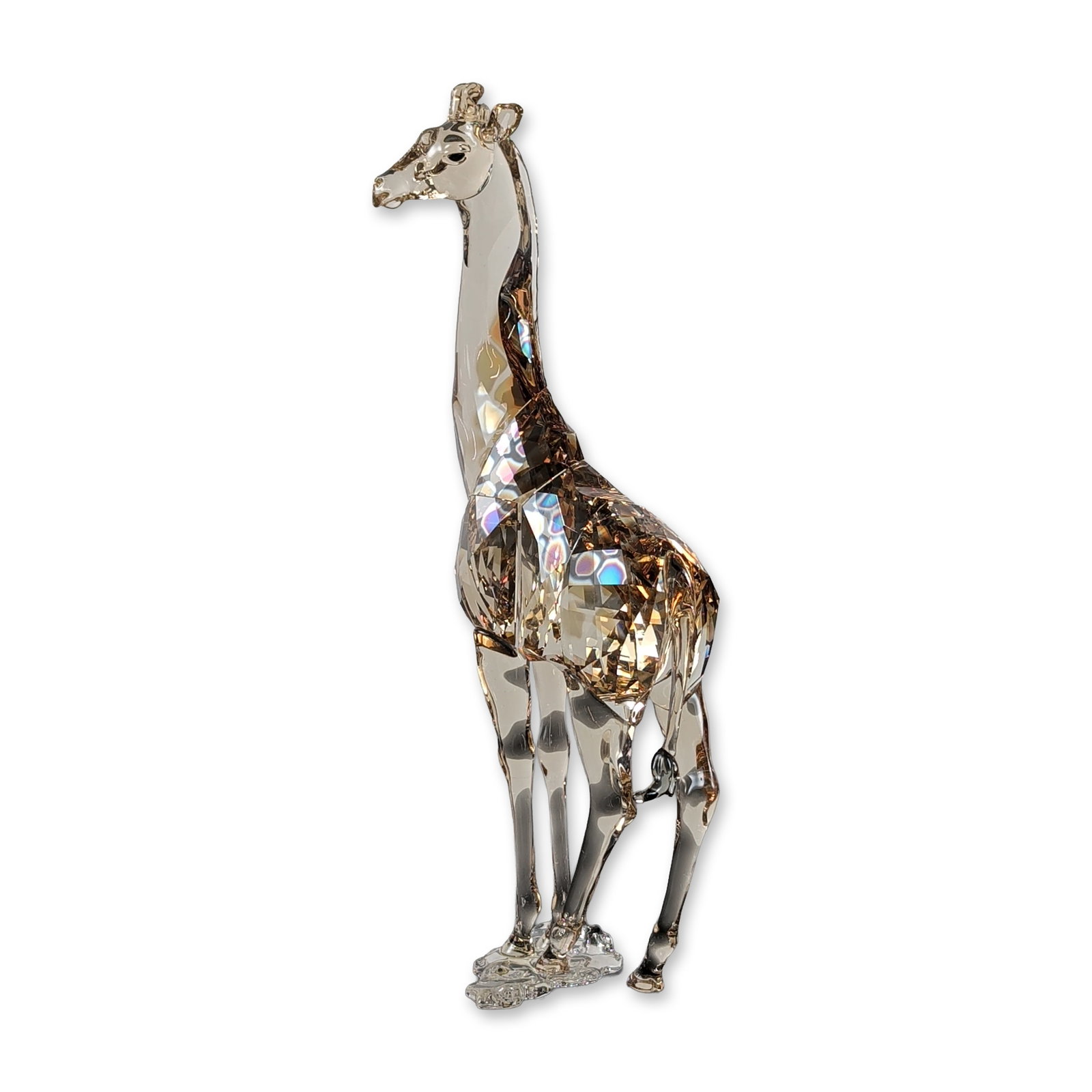 Swarovski Mudiwa Crystal Giraffe Figurine: Swarovski. Figurine in faceted lead crystal titled Mudiwa, designed by Martin Zendron. The stylized standing figure features a multi-toned cognac and golden-brown body with a clear crystal neck and ba