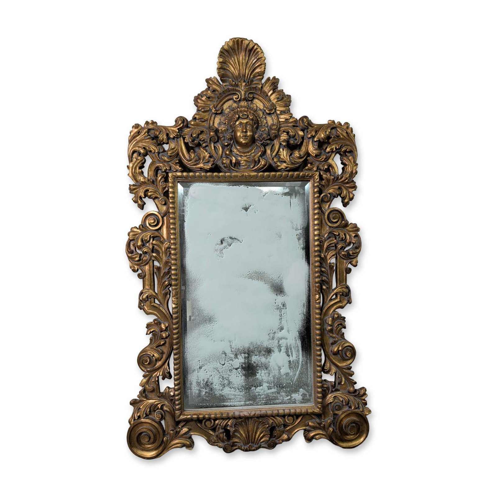Large Baroque Style Gilt Wall Mirror: Large wall mirror in the Baroque revival style. The frame is constructed of carved wood with a gilded finish. The ornamentation features a prominent top crest with a classical mascaron centered among 