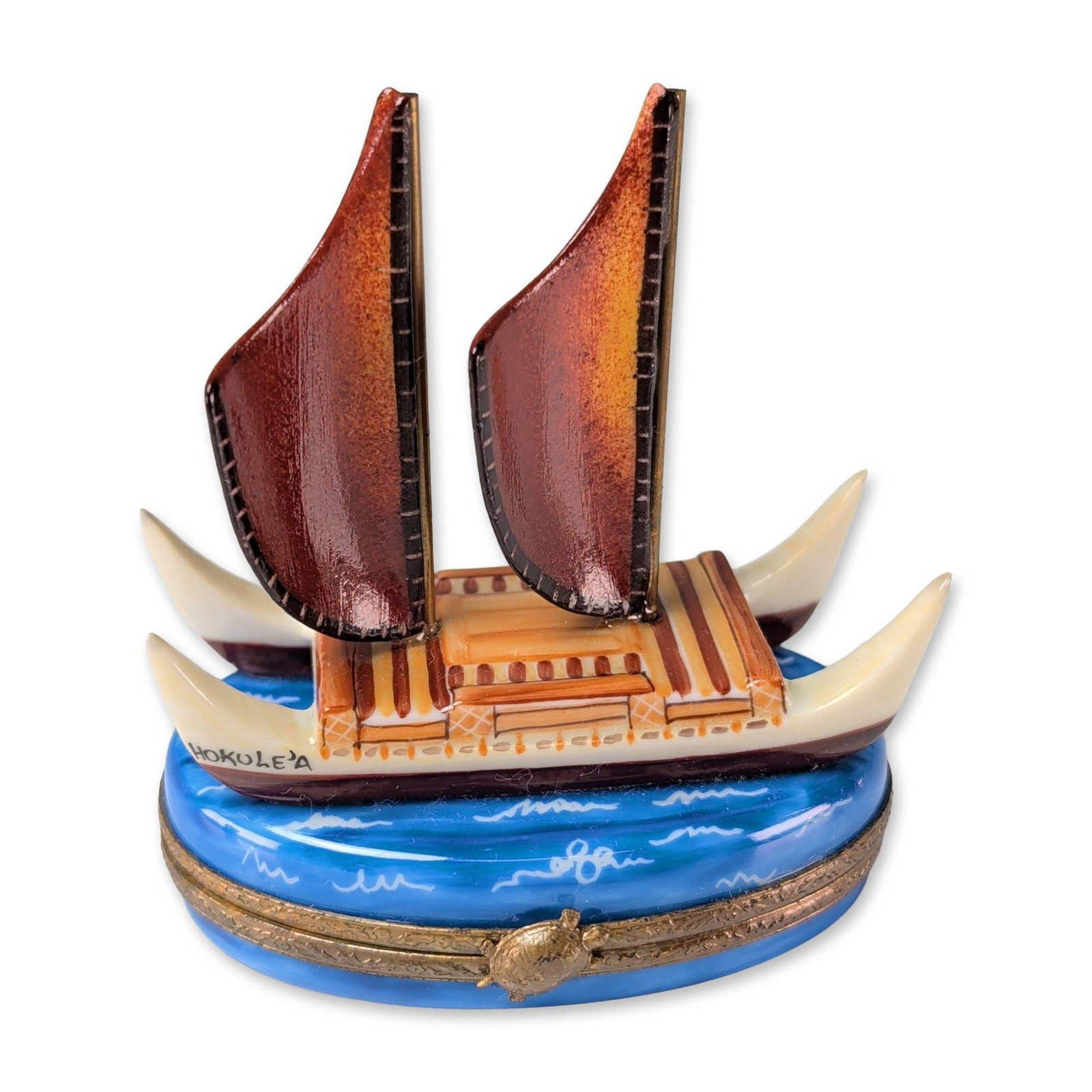 Limoges Peint Main Hokule'a Trinket Box: Limoges, France. Hand-painted porcelain hinged trinket box modeled as the Hawaiian voyaging canoe Hokule'a. The double-hulled vessel features two crab-claw sails in ochre and brown tones with four whi