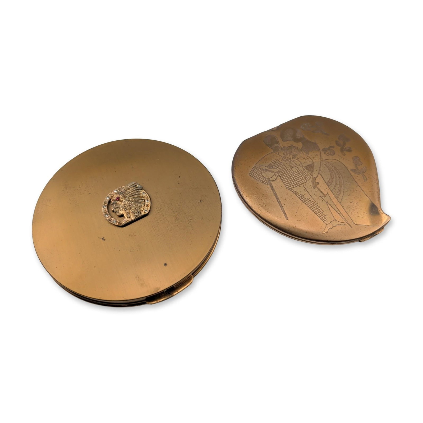 Two Dorset Fifth Avenue and Elgin American Powder Compacts: Two mid-century American powder compacts in gold-toned metal. The first is a round Dorset Fifth Avenue example featuring a central applied Native American profile emblem in a feathered headdress,