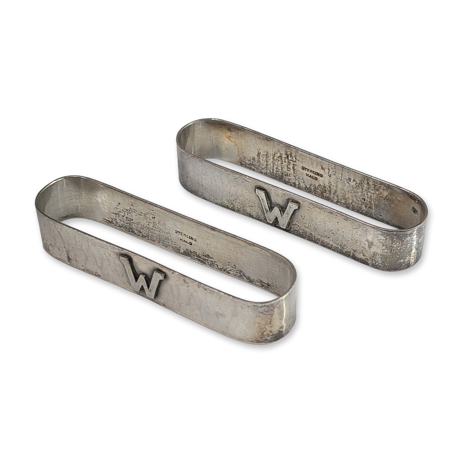 Pair of Kalo Sterling Silver Napkin Rings: Each hand-wrought sterling silver ring features an oblong form with a hammered texture and an applied block letter W. The reverse of one ring is engraved with the name David, while the second is engra