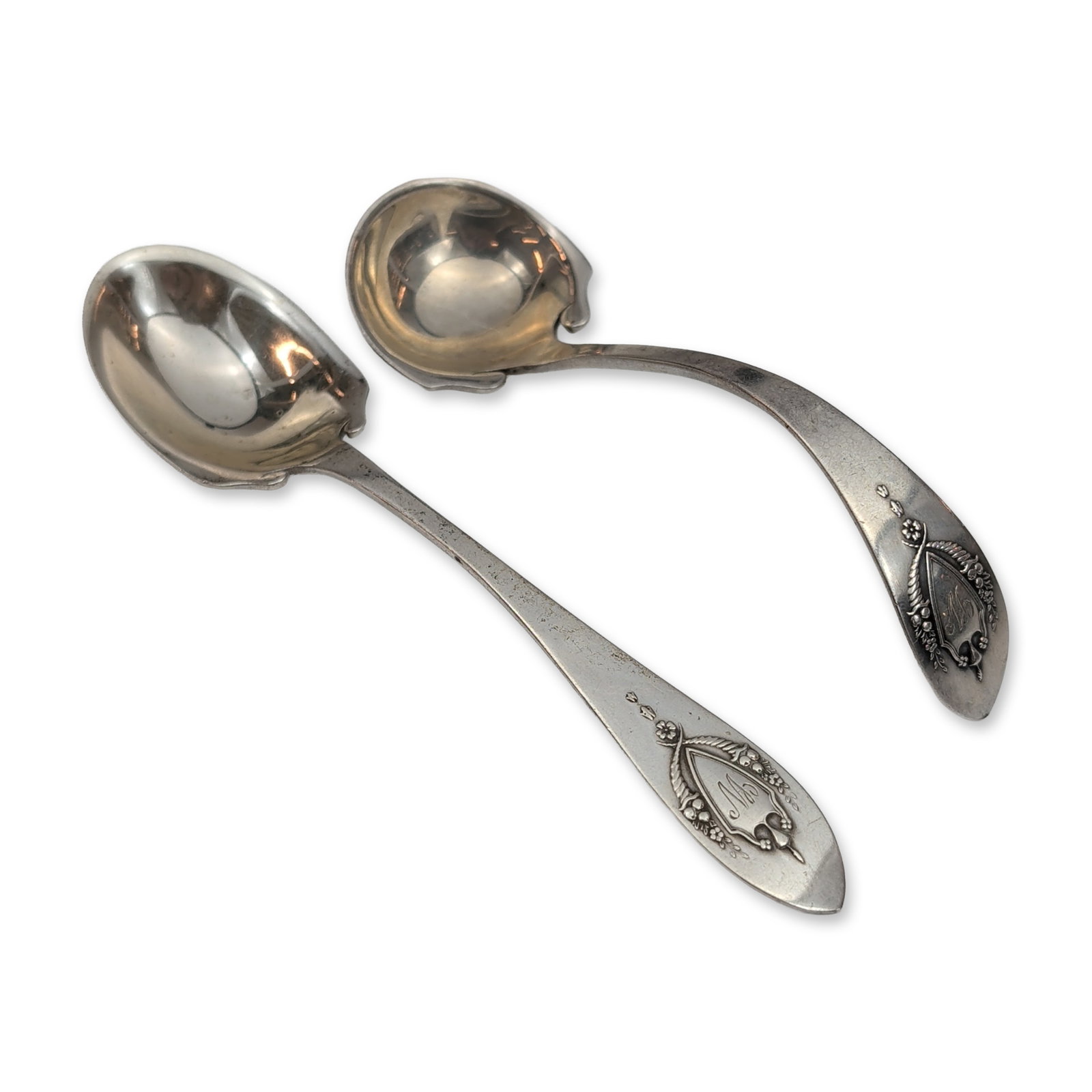 Pair of Lunt Sterling Silver Spoons: Both pieces feature fluted scalloped bowls and handles decorated with foliate scrolls, floral sprays, and a central shield cartouche. Stamped to the reverse with Sterling. Dimensions: 6"W x 1.25"H. We