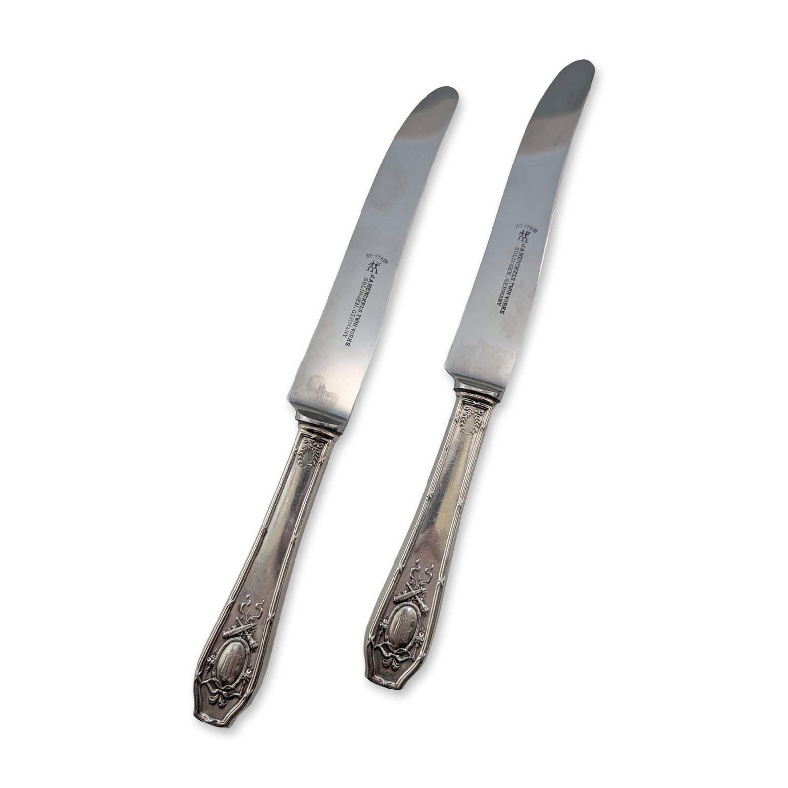 Pair of R. Wallace & Sons Sterling Silver Dinner Knives: Pair of knives featuring sterling silver weighted handles and stainless steel blades. The handles exhibit Neoclassical motifs including laurel wreaths at the bolsters and terminals decorated with ribb