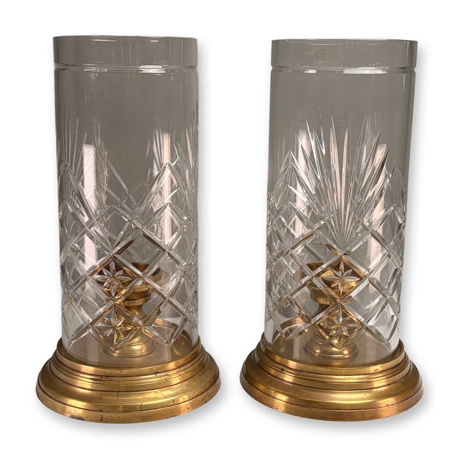 Pair of Ajka Hungarian Lead Crystal and Brass Hurricane Lamps: A pair of two-piece hurricane candleholders in 24 percent lead crystal and turned brass. The hand-cut crystal shade features a repeating diamond crosshatch pattern with inset star motifs above a starb