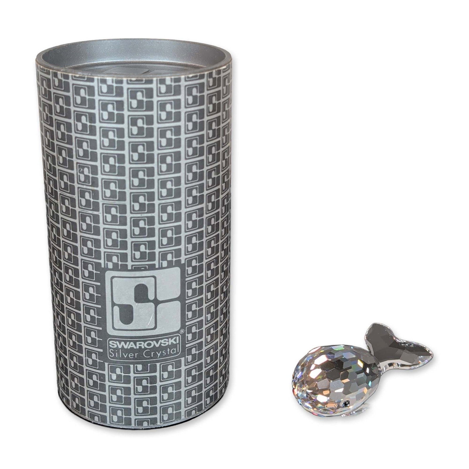 Swarovski Silver Crystal Whale Figurine: The piece features a multi-faceted body with smooth clear crystal tail fluke and side fins, accented with inset dark cabochon eyes. The underside of the body bears a hand-etched signature Michael Stam