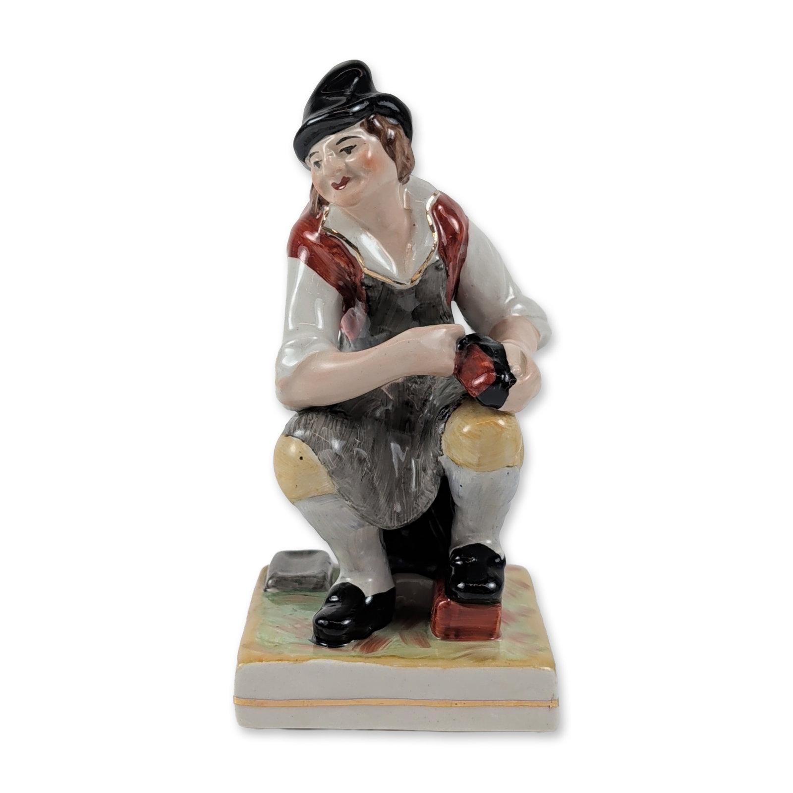 William Kent Staffordshire Pottery Cobbler Figurine: William Kent (Porcelains) Ltd. polychrome glazed ceramic figurine depicting a seated cobbler engaged in his craft. The figure is modeled in 19th-century style attire featuring a black tricorn hat, red