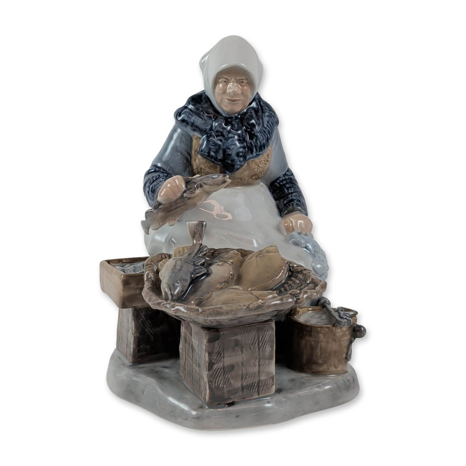 Bing and Grondahl Axel Locher Fish Market Figure: The Bing and Grondahl porcelain figure, titled Fish Market and designed by Axel Locher, features a polychrome glazed finish. It depicts a woman in traditional dress seated among baskets and crates of 