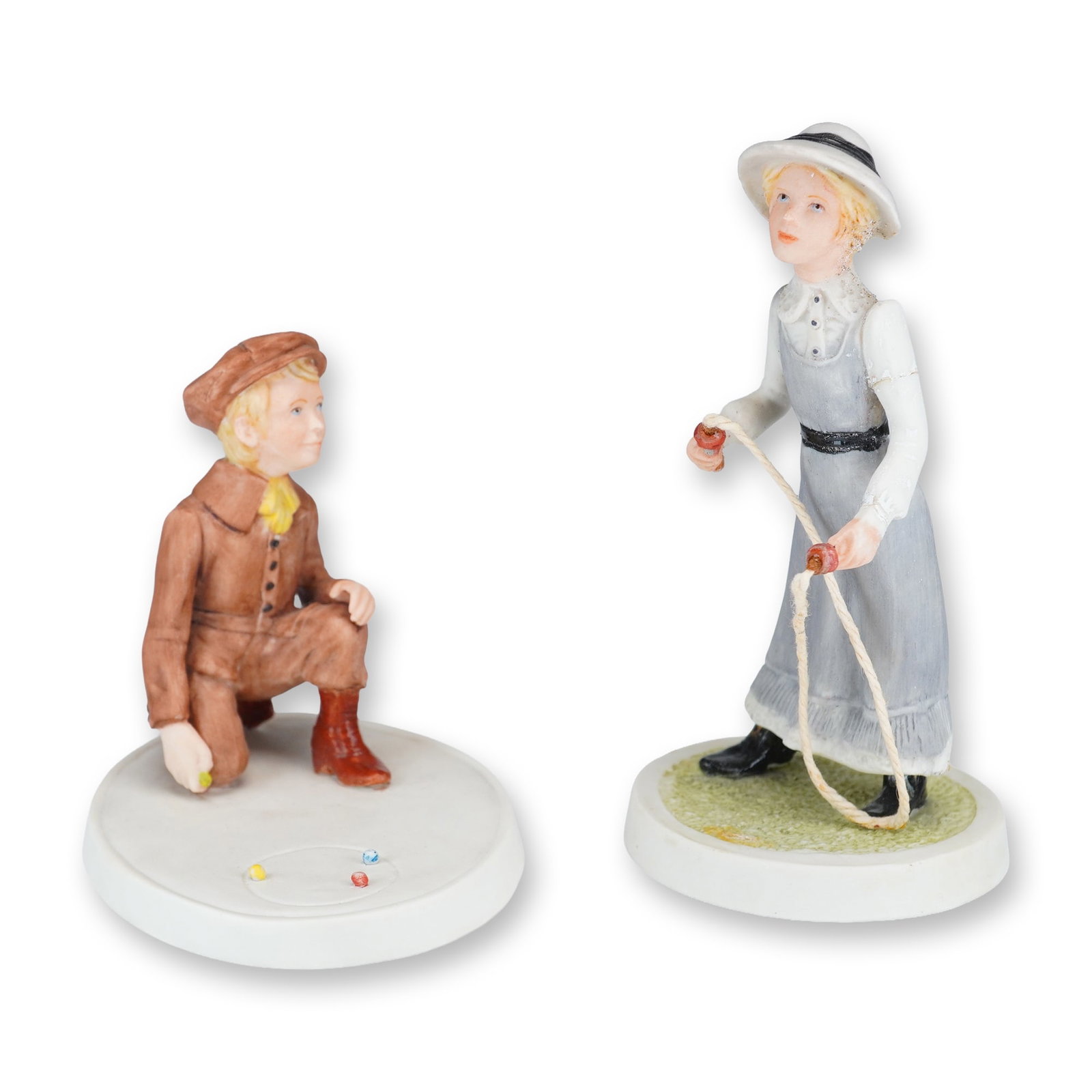 2pc Wedgwood Porcelain Figurines, Victorian Series: This pair of Wedgwood hand-painted porcelain figurines from a Victorian series depicts children at play. The first figurine features a boy kneeling on an oval base while playing a game of marbles. He 