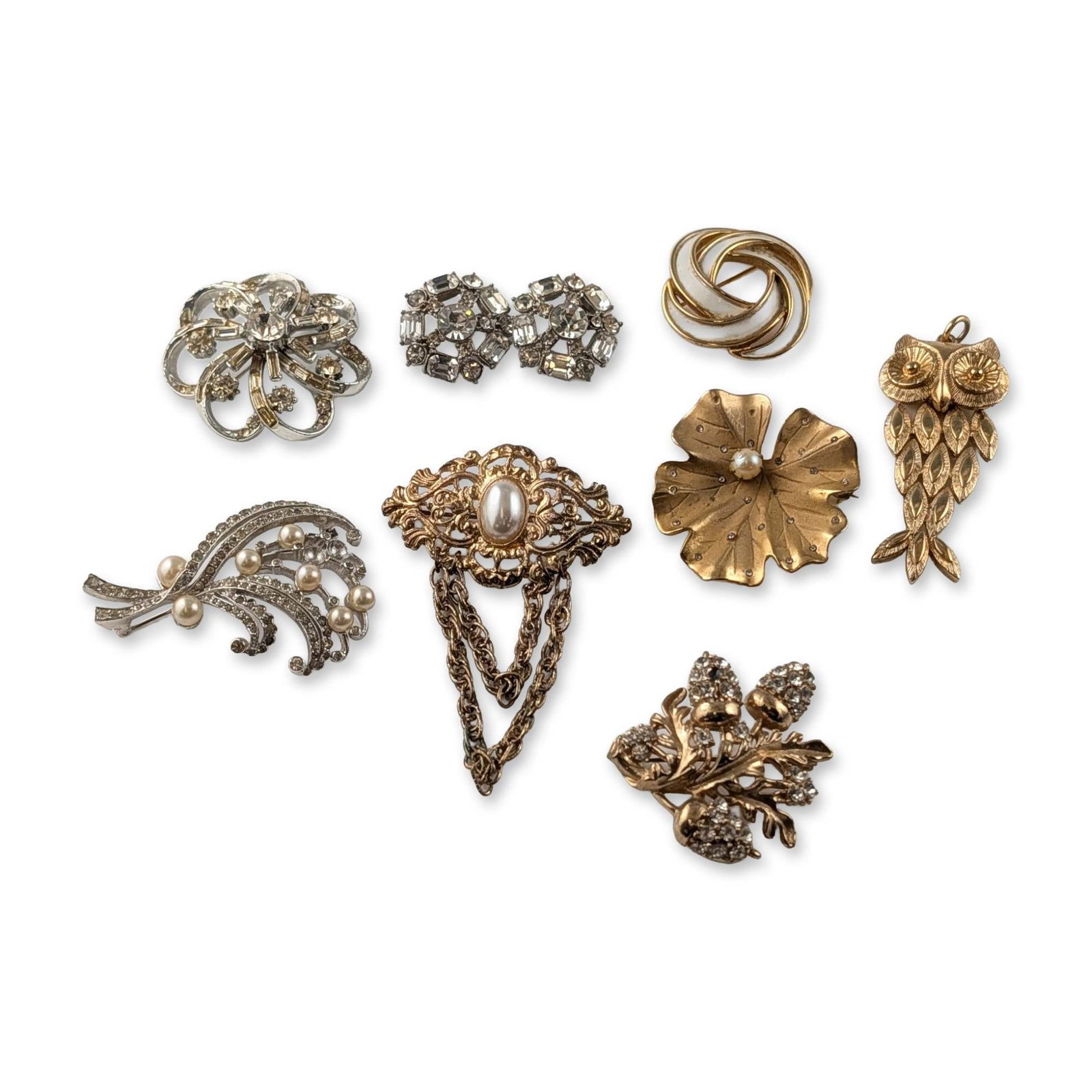 9pc Grouping of Trifari Coro and Avon Brooches: Mid-century and Victorian Revival style. Collection of costume jewelry brooches in gold-tone and silver-tone base metals, featuring clear rhinestones, faux pearls, and enamel accents. The group includ