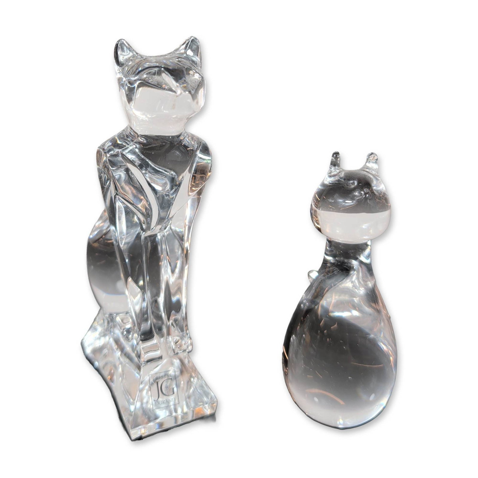 Two J.G. Durand and Mila Signed Glass Cat Figurines: Two cat figurines in clear glass and crystal. One example by J.G. Durand (France) featuring a stylized, geometric Egyptian seated form with faceted edges, marked with the manufacturer logo to the base