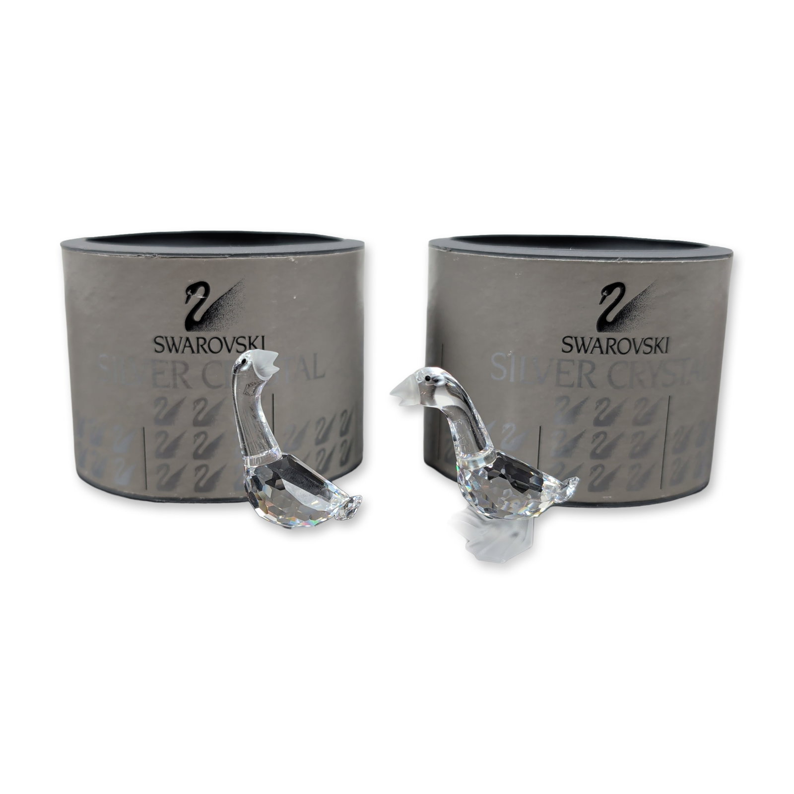 Swarovski Silver Crystal Pair of Gosling Figurines: Crafted in faceted clear lead crystal, this set of two features frosted crystal beaks and webbed feet. It includes one figurine with a raised head and another with a level head. Each bears the acid-et