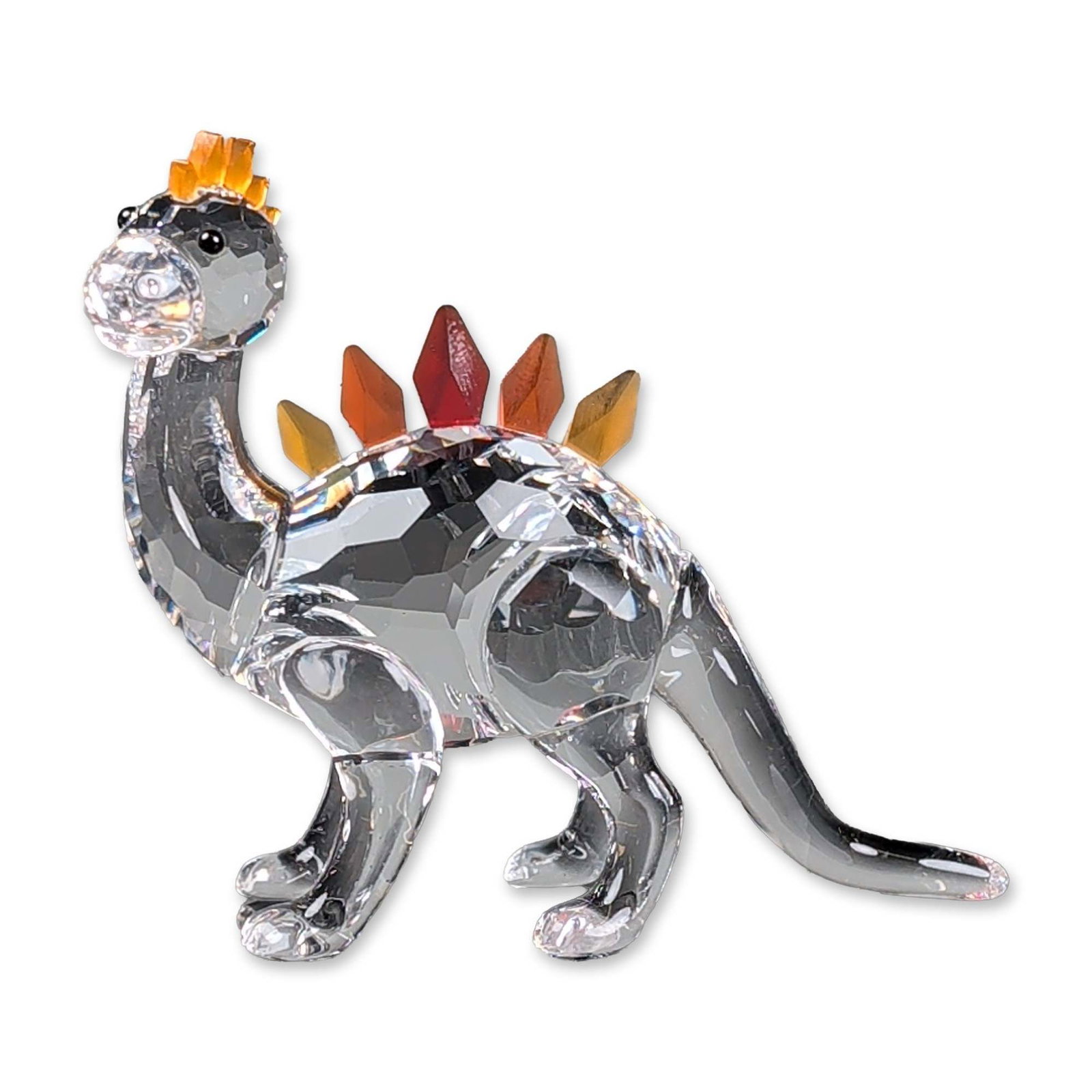 Swarovski Crystal Figurine, Dino Dinosaur: Part of the Swarovski Fairy Tales collection. Dino Dinosaur figurine is faceted clear lead crystal with graduated amber, orange, and red crystal plates along the back. The figure is depicted in a play