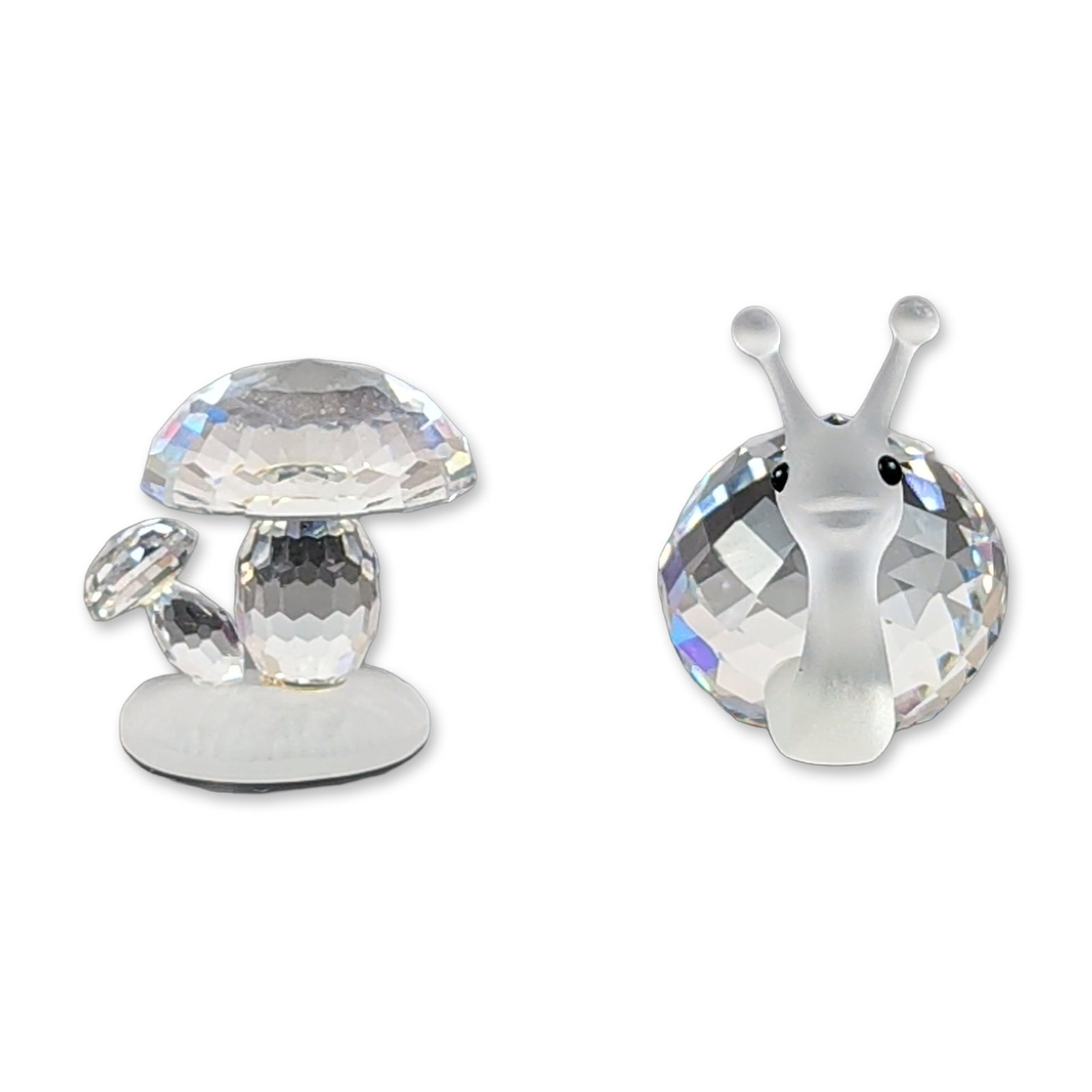 2pc Swarovski Silver Crystal Snail and Mushroom Figurines: Two figurines in faceted and frosted lead crystal from the Silver Crystal collection. The snail features a frosted head and neck with black crystal eyes and a multi-faceted clear crystal shell. The mu