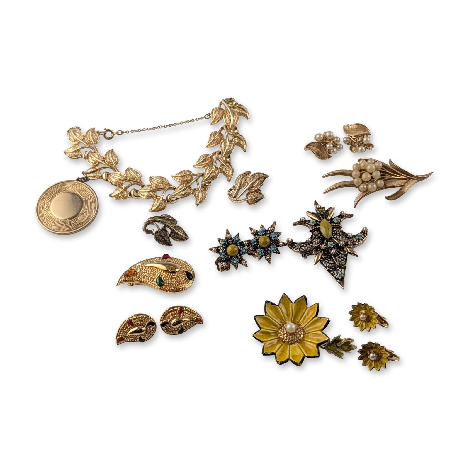 15pc Group of Mid-Century Trifari Coro and Avon Costume Jewelry: Mid-century. Assorted costume jewelry including brooches, earrings, and bracelet. The collection features botanical and celestial motifs such as a leaf-link bracelet with circular pendant, a starburst