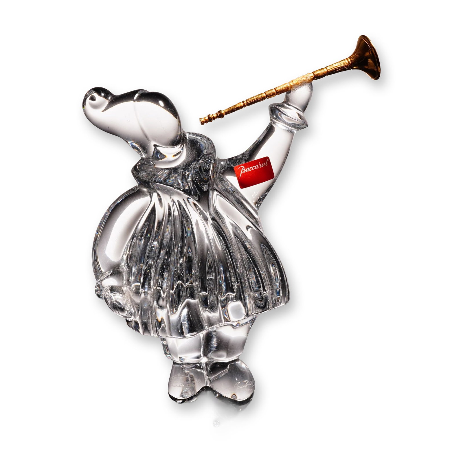 Baccarat by Jean Boggio Crystal Masquerade Trumpeter Figurine: The piece depicts a stylized anthropomorphic elephant, characterized as a trumpet angel, standing in a vertically ribbed garment with a ruffed collar. The figure holds a gold-toned metal trumpet to it