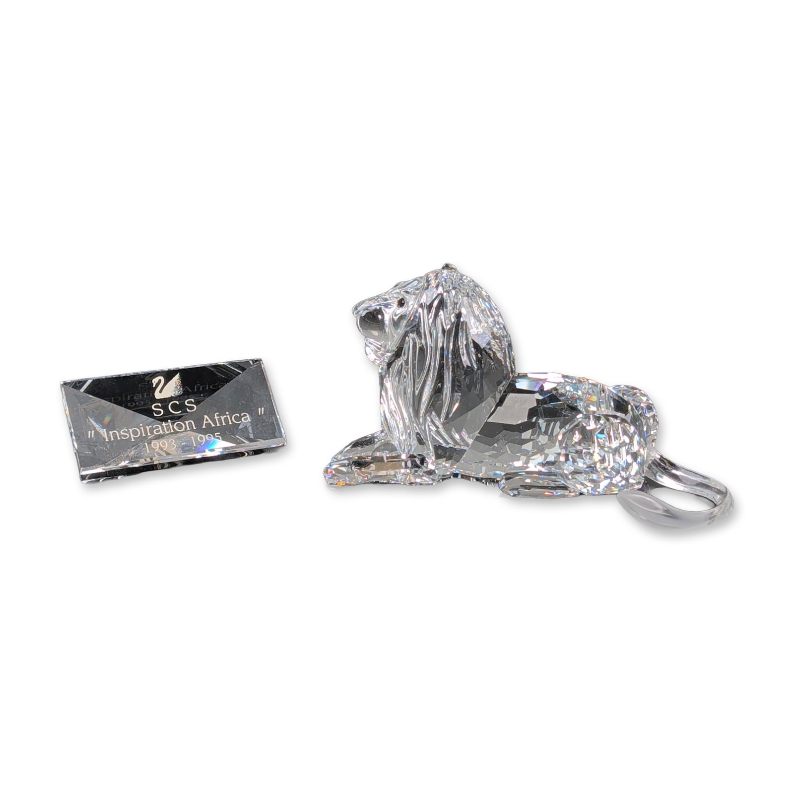 2pc Swarovski Crystal 1995 Annual Edition Figurine, African Lion and Title Plaque: Swarovski Crystal Society (SCS) 1995 Annual Edition figurine from the Inspiration Africa series, depicting a seated male lion. Faceted clear lead crystal construction with textured frosted crystal man