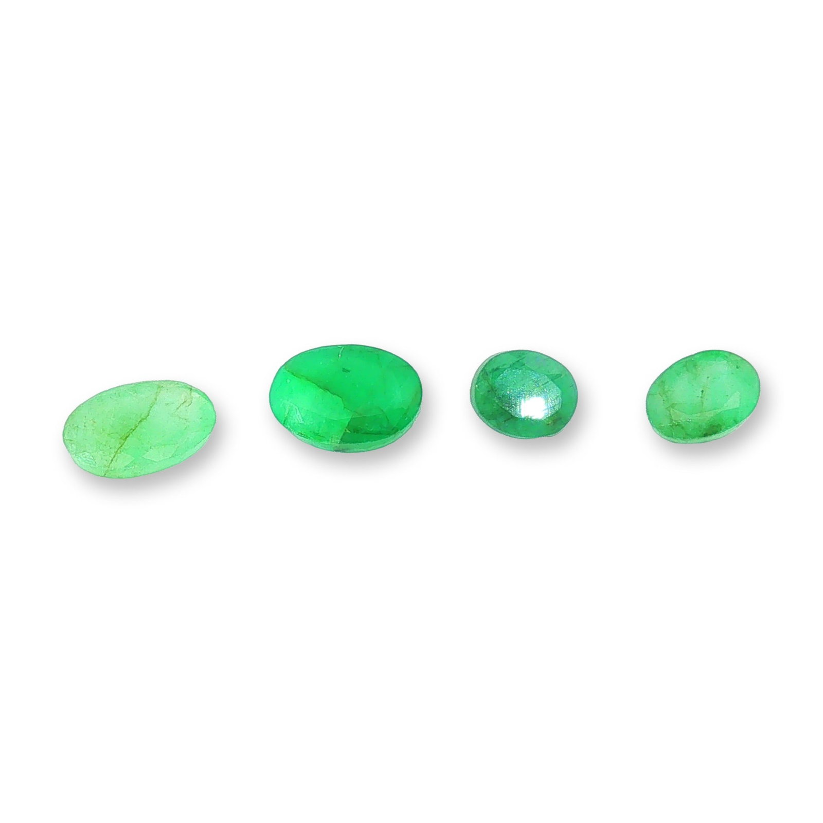 Four Loose Oval Cut Emeralds: Collection of four loose green gemstones appearing to be natural emeralds. Each stone features an oval faceted cut, showcasing a vibrant green hue with varying color intensities. The collection presen
