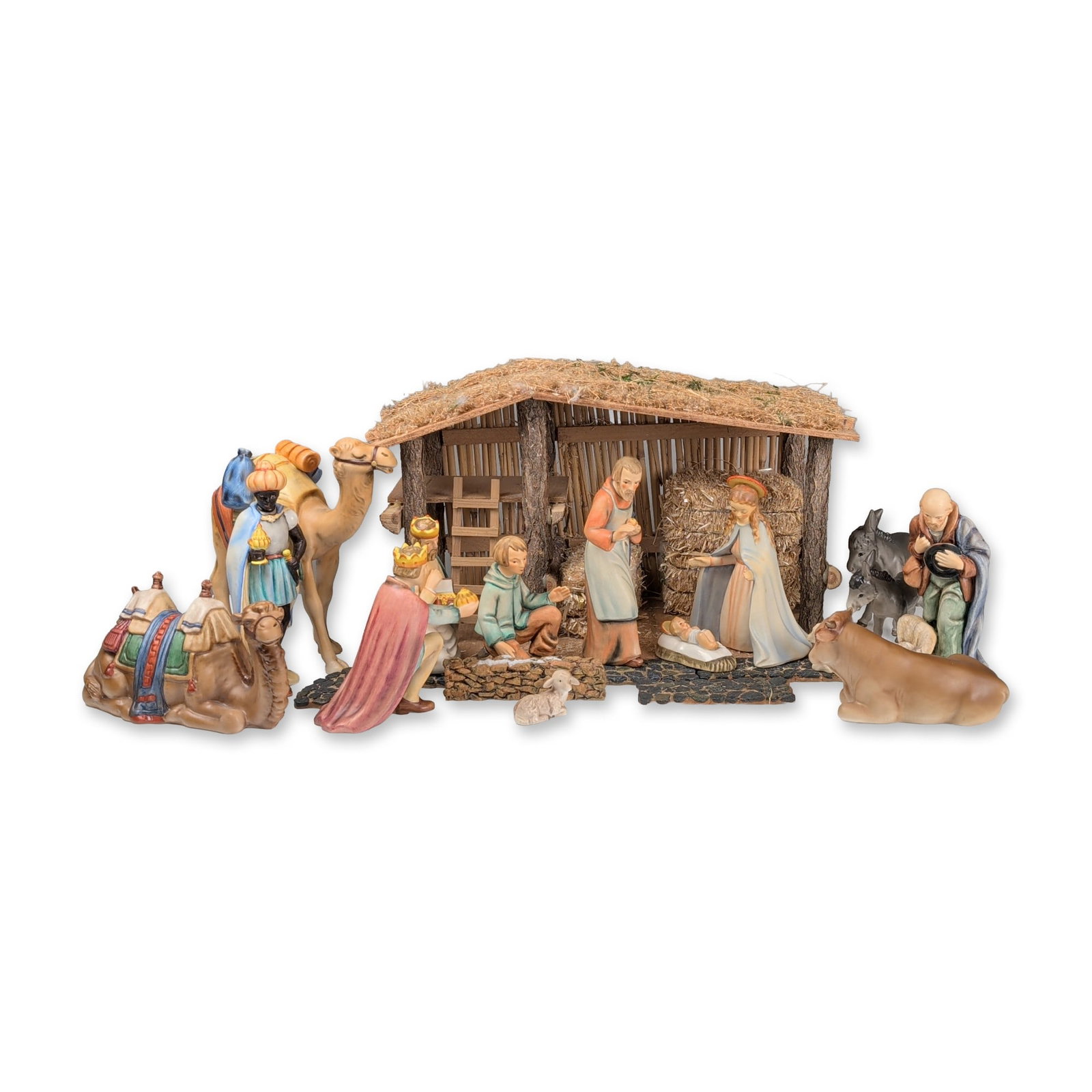 25pc Goebel Hummel Porcelain Nativity Set and Stable: Goebel Hummel, West Germany. Nativity set in hand-painted ceramic with a matte finish, accompanied by a rustic wooden and straw-thatched stable. The collection includes a group of figurines: the Holy 
