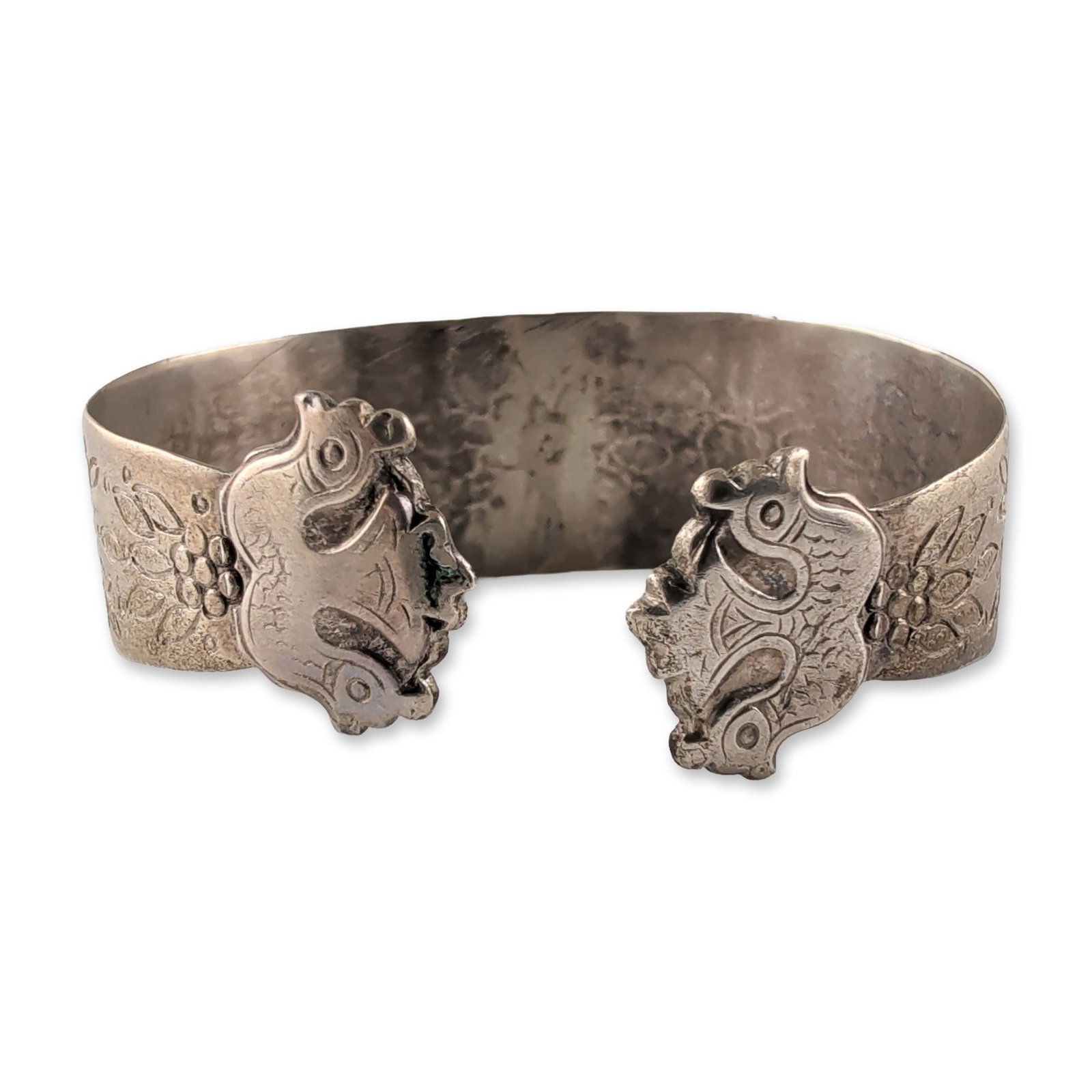 Southeast Asian Folk Art Style Sterling Silver Cuff Bracelet: Featuring intricate chased and repousse ornamentation. The band is decorated with floral and foliate motifs against a stippled background. The terminals are fashioned into stylized bird heads meeting 