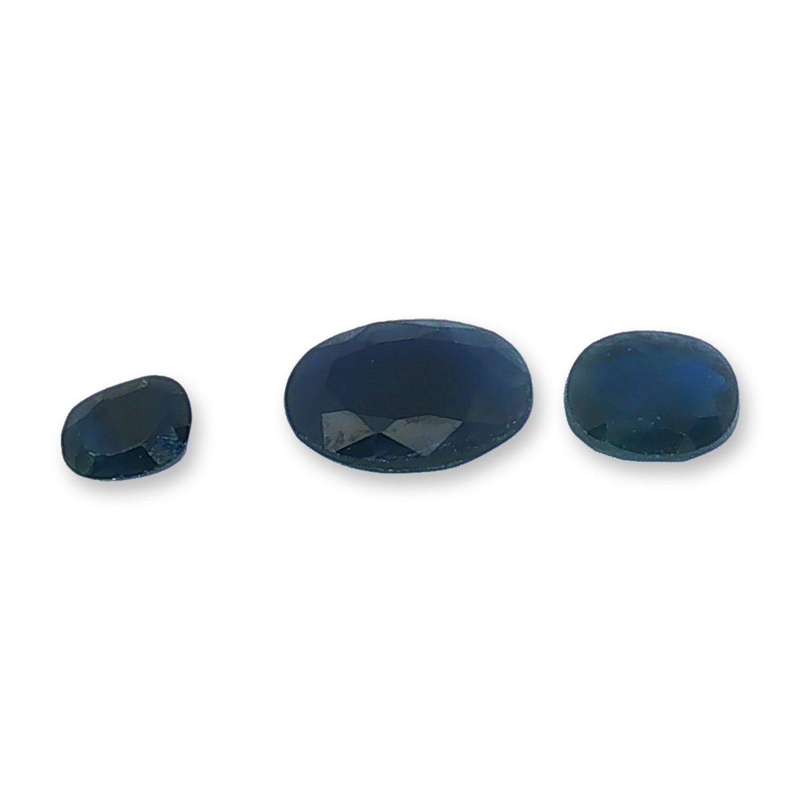 Trio of Loose Royal Blue Oval Cut Sapphires: Trio of loose gemstones, appearing to be blue sapphires, featuring an oval faceted cut. The stones exhibit a deep navy blue hue with flashes of royal blue, presented in a graduated three-piece set.