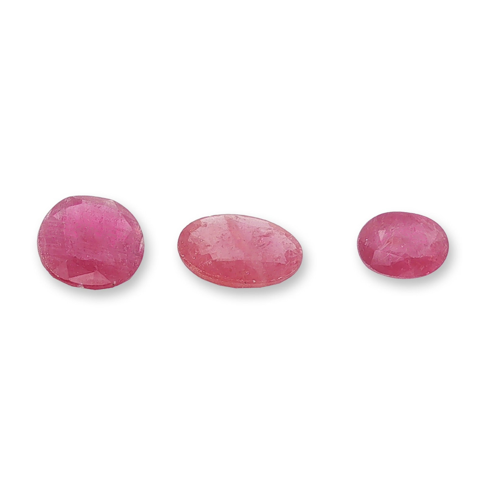 Three Oval Cut Purplish Red Loose Rubies: Three loose gemstones, appearing to be rubies, featuring a vibrant purplish-red hue and oval faceted cuts. Each gemstone displays visible internal inclusions including fractures, clouds, and potential