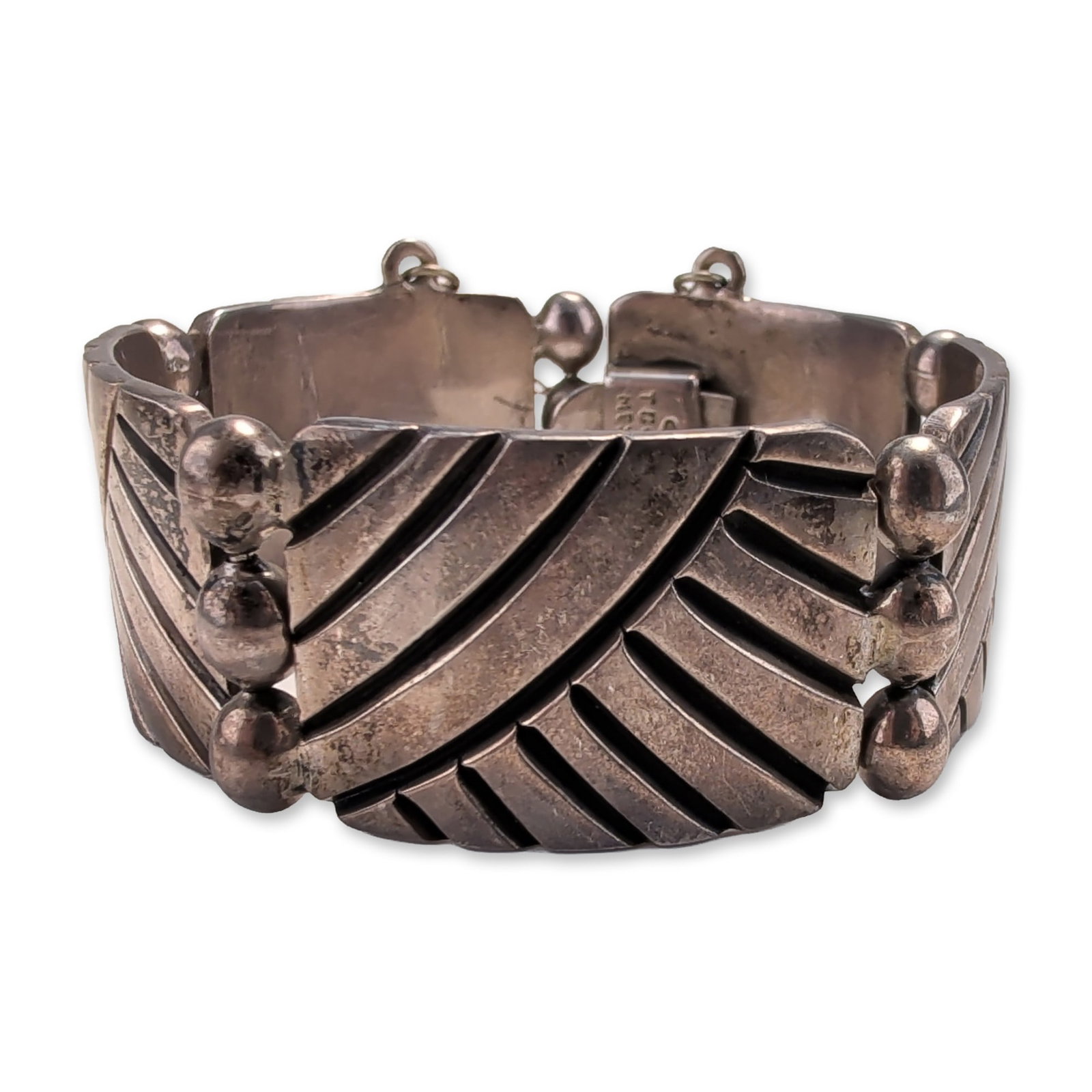Taxco Mexico Sterling Silver Modernist Link Bracelet: Post-1979 Taxco, Mexico. Link bracelet in sterling silver, featuring wide rectangular panels decorated with deep diagonal geometric grooves and bordered by raised spheres at the hinges. Secured by a t