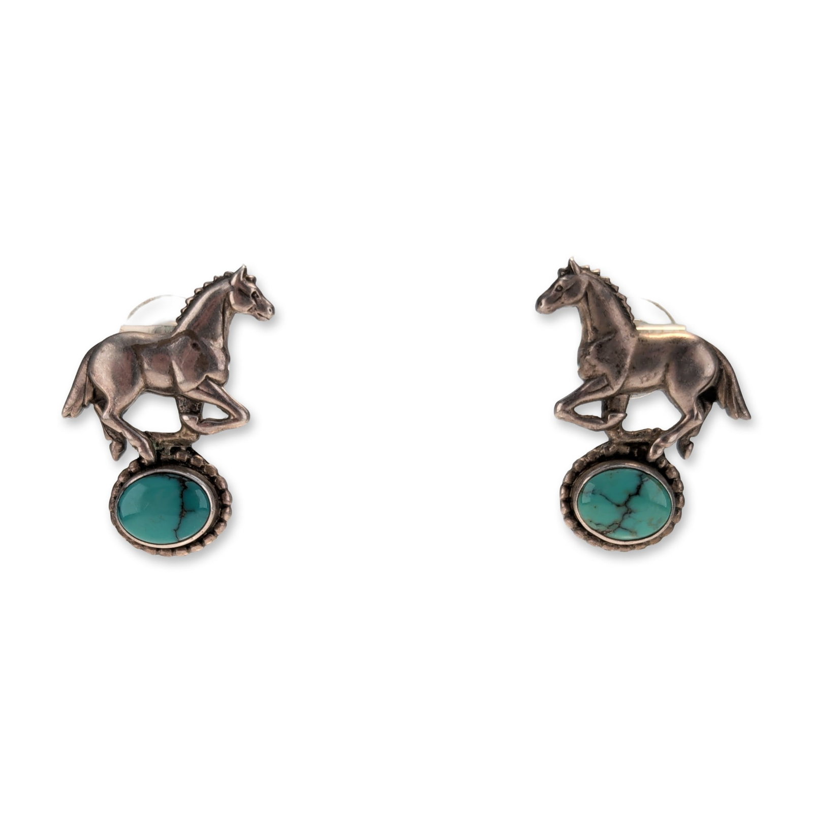 Pair of Sterling Silver Turquoise Horse Earrings: Pair of sterling silver stud earrings in a Southwestern equestrian style. Each earring features a cast leaping horse figure positioned above an oval turquoise cabochon. The gemstones are secured in sa