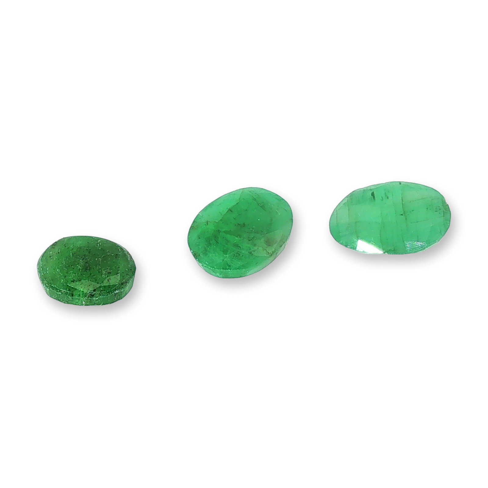 Trio of Oval Cut Loose Emeralds: Trio of loose emeralds appearing to be natural, each shaped into a classic oval faceted cut. These unmounted gemstones display varying shades of characteristic green, ranging from deep forest green to