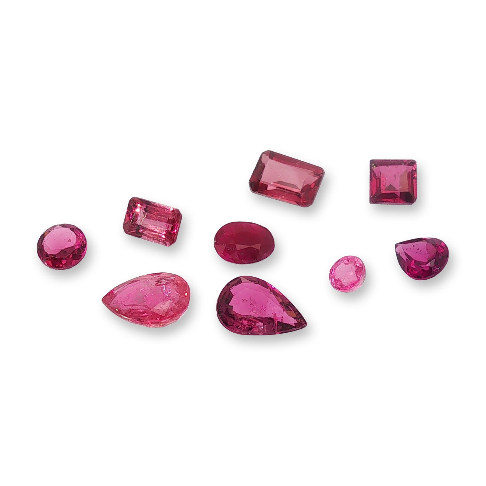 Collection of Nine Mixed Cut Loose Rubellite Gemstones: Collection of nine loose gemstones appearing to be rubellite tourmaline in a rich spectrum of pinkish-red hues. The assortment features a variety of classic shapes including three emerald step cuts,