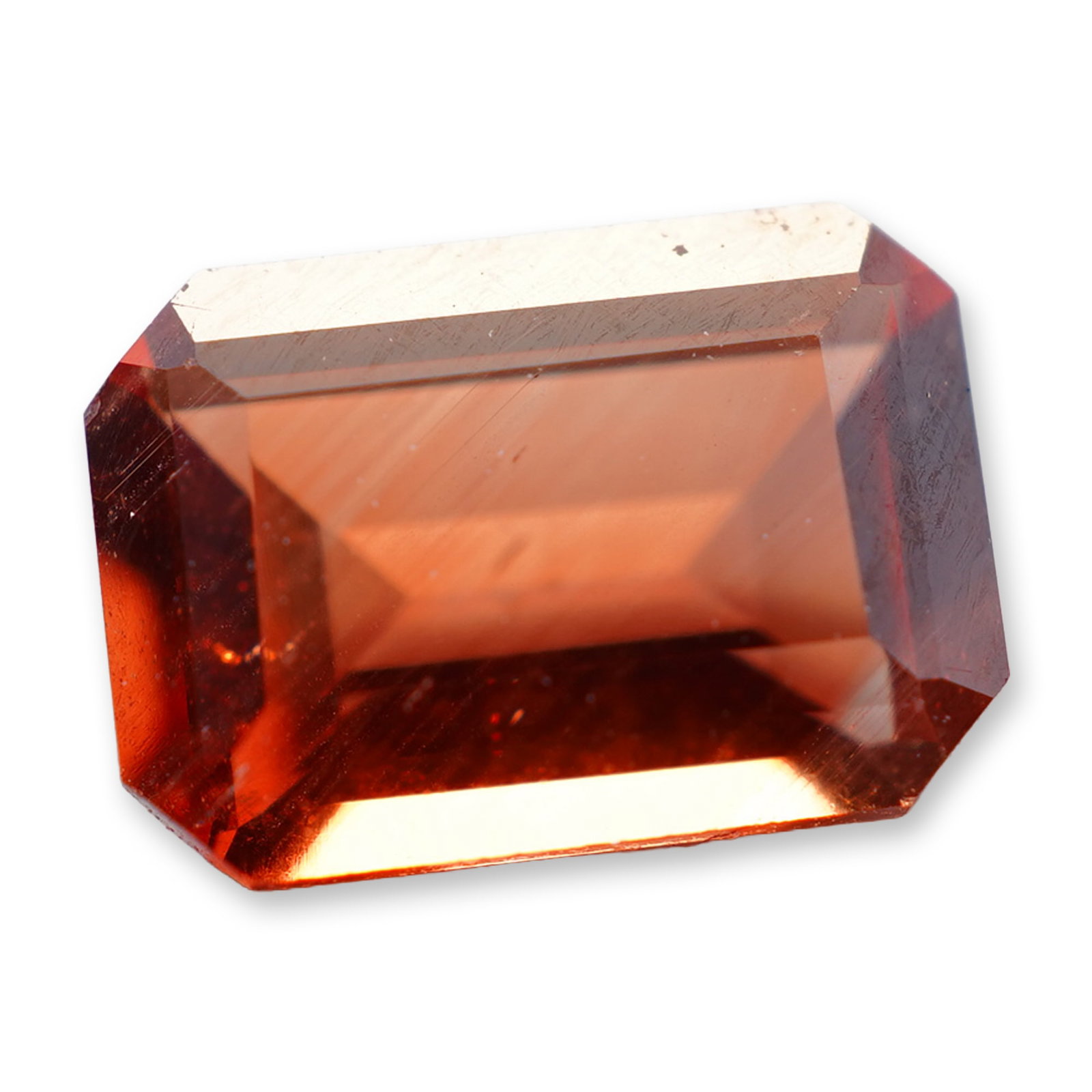 Loose Emerald Cut Orange Labradorite: Loose faceted gemstone in labradorite, featuring an emerald cut with clipped corners. The stone exhibits a saturated orange to reddish-orange hue. Internal crystalline inclusions and veining are visib