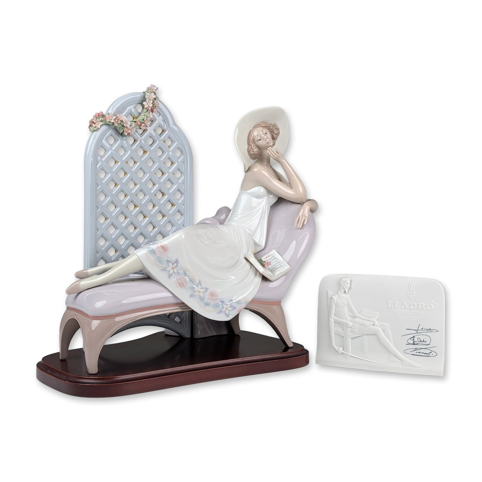 2pc Lladro Porcelain Figurines, Garden of Dreams 01007634 with Base and CS Plaque: Garden of Dreams depicts a woman in a sunhat reclining on a chaise longue with an open book, positioned in front of a lattice screen with hand-applied porcelain flowers. The underside features the blu
