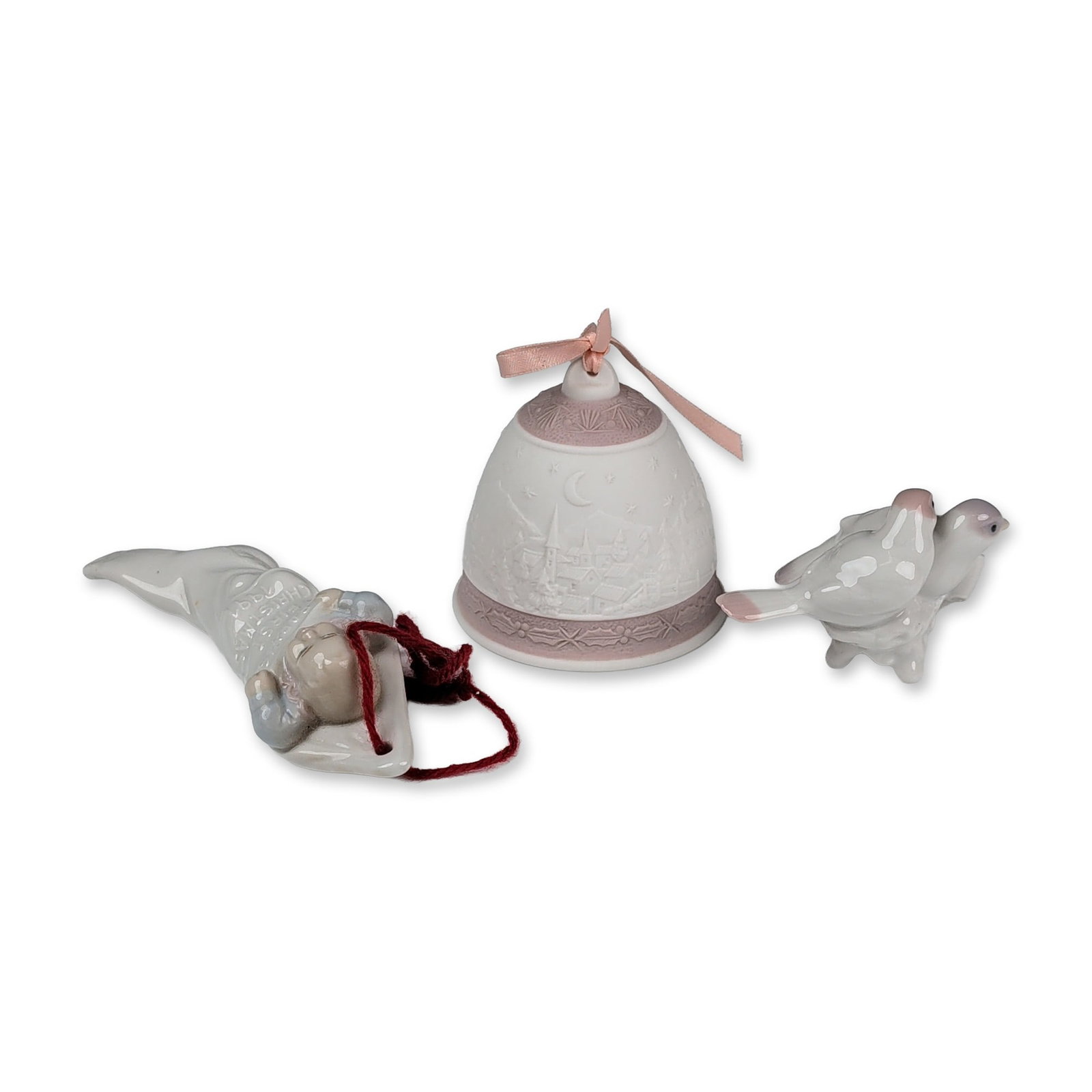 3pc Lladro Porcelain Glazed and Bisque Ornaments: The collection consists of a pink-toned bisque annual bell with relief-molded scenes of the Nativity and a winter village, a glazed First Christmas Together 1991 bird figurine, and a glazed Baby's Fir