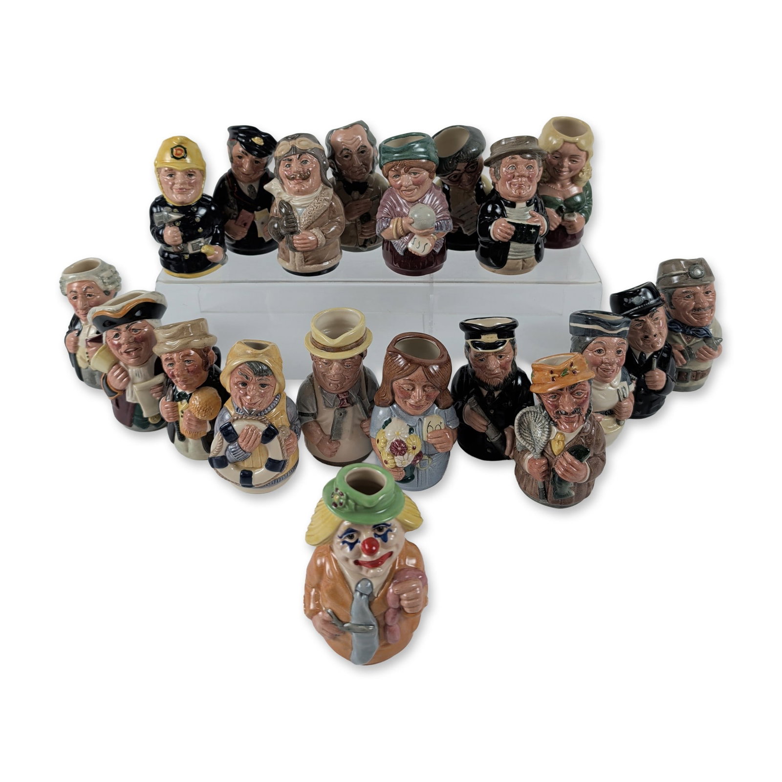 Group of 19 Royal Doulton Doultonville Collection Character Jugs: Royal Doulton, England. Group of nineteen character jugs from the Doultonville Collection in hand-painted glazed ceramic. The series features stylized figural busts representing various town