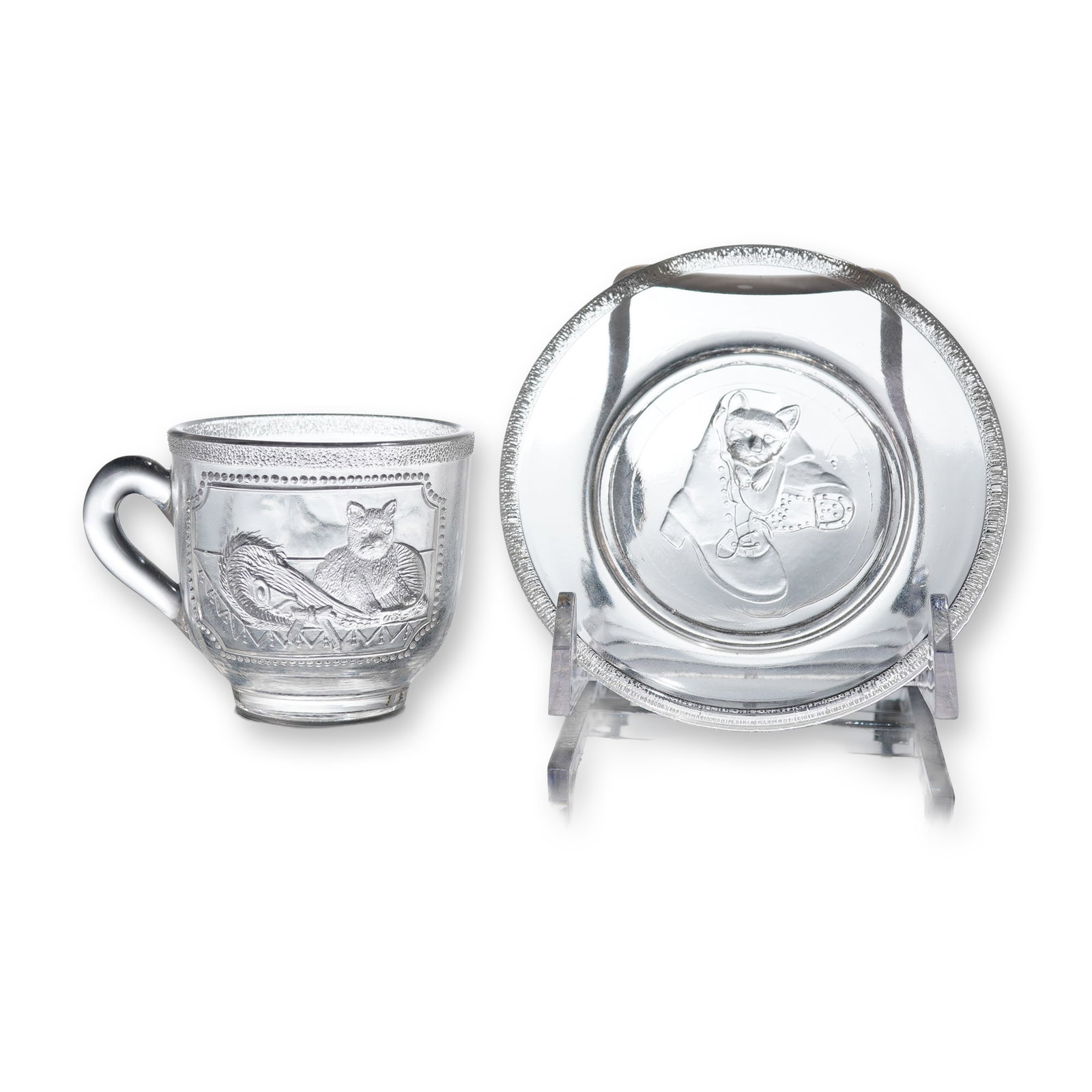 EAPG Cat on a Cushion Pattern Child's Cup and Saucer Set: This lot consists of a small cup and saucer set, comprising two items, executed in clear pressed glass and identified as the Early American Pattern Glass (EAPG) Cat on a Cushion pattern. This small
