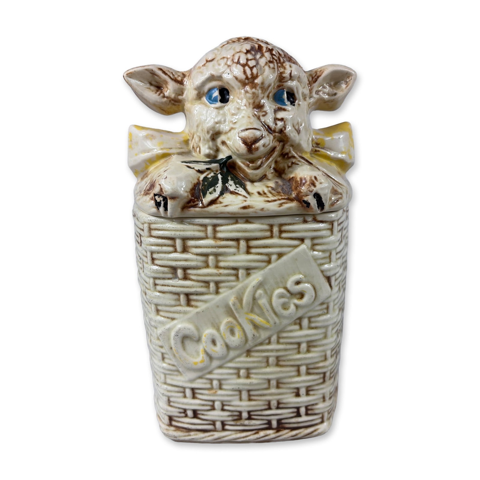 McCoy Pottery Lamb in Basket Cookie Jar: McCoy Pottery figural cookie jar in glazed earthenware, featuring a lid modeled as a lamb's head with a yellow bow and a green leaf in its mouth. The rectangular base is designed with a relief-molded 
